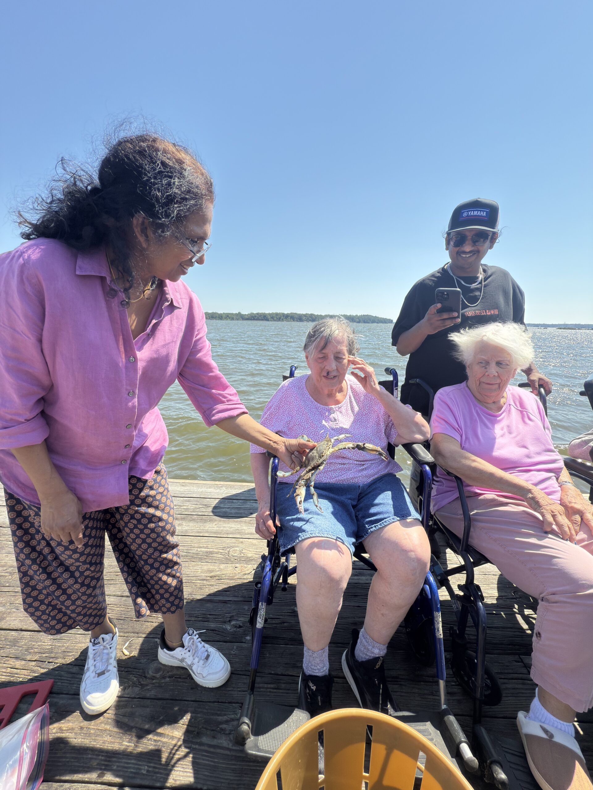People relaxing in wheelchairs by the ocean on a sunny day, with one person standing beside them