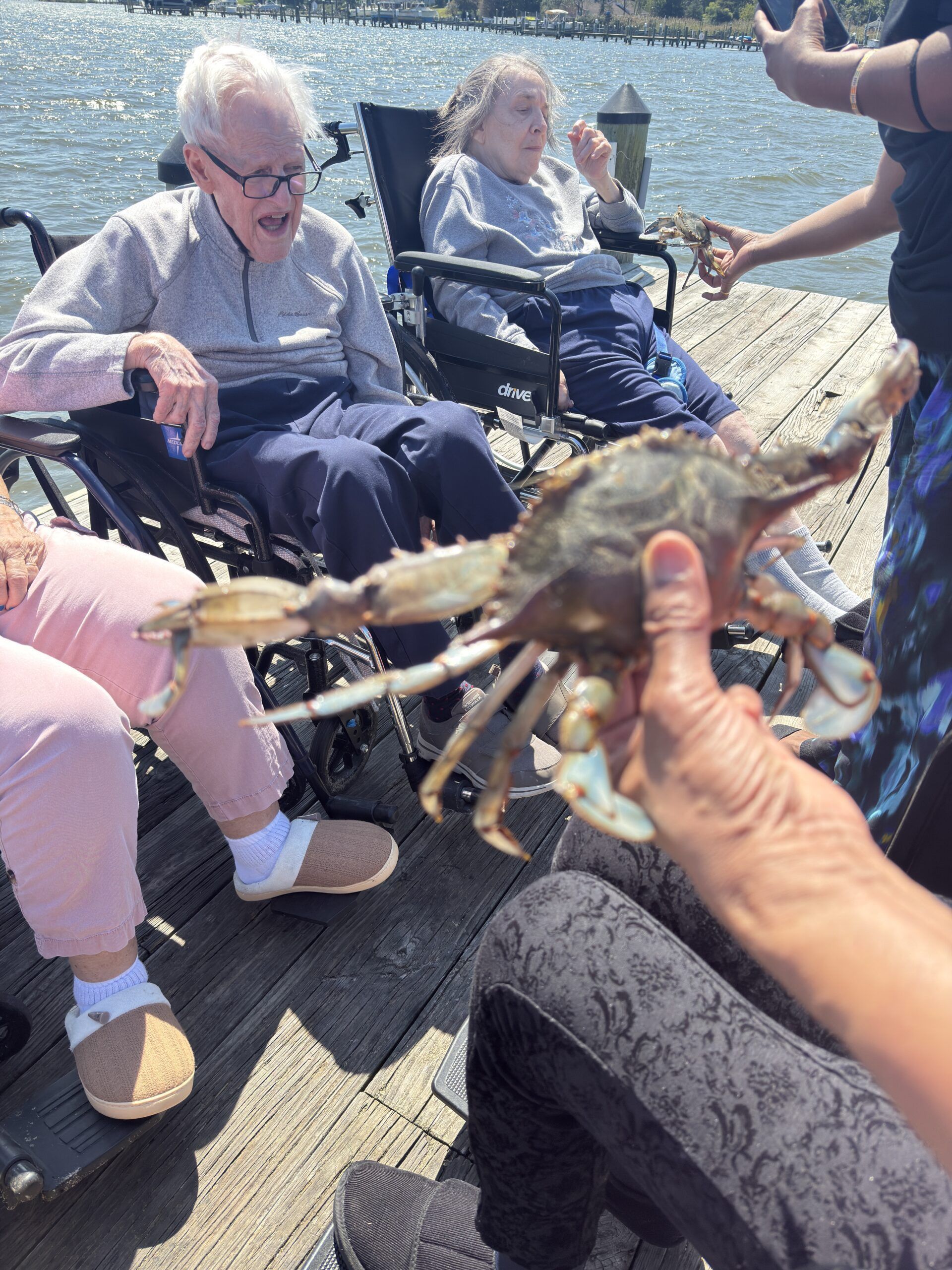 Person holding a crab shell toward seated people on a dock by the water