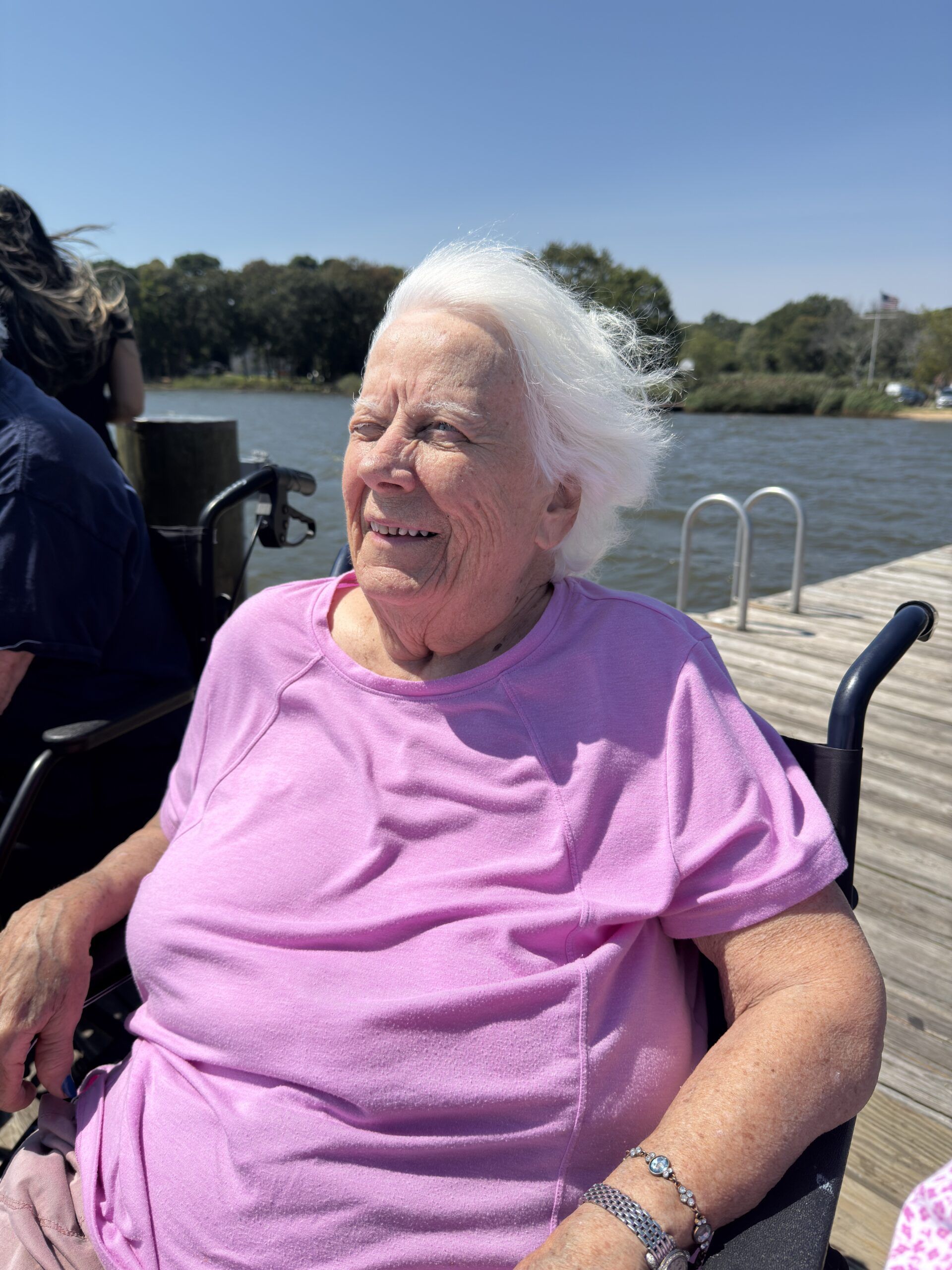Smiling woman in a purple shirt sitting on a dock by the water on a sunny day