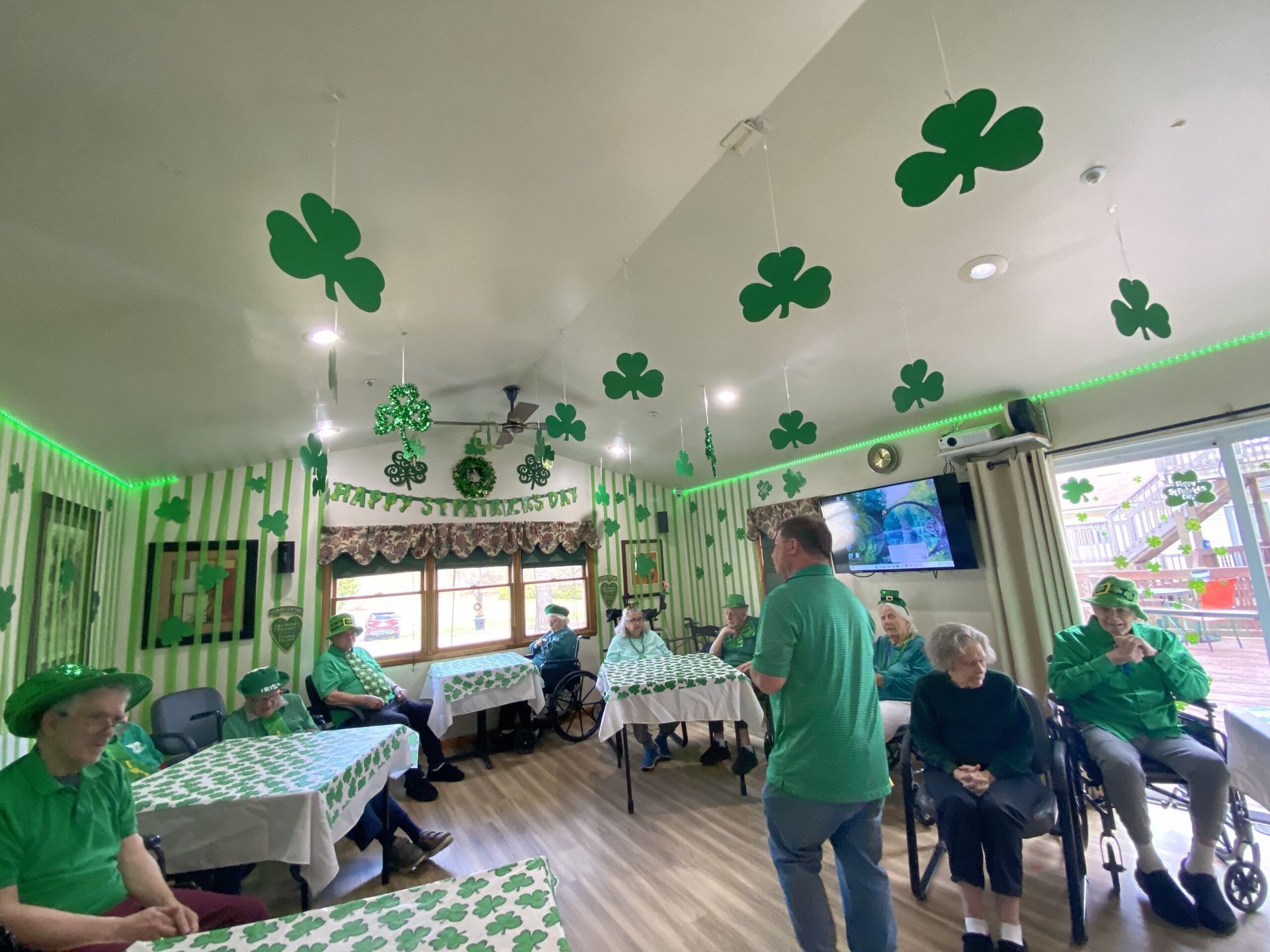 People in green shirts and shamrock decorations gather in a bright room at a St. Patrick’s Day celebration
