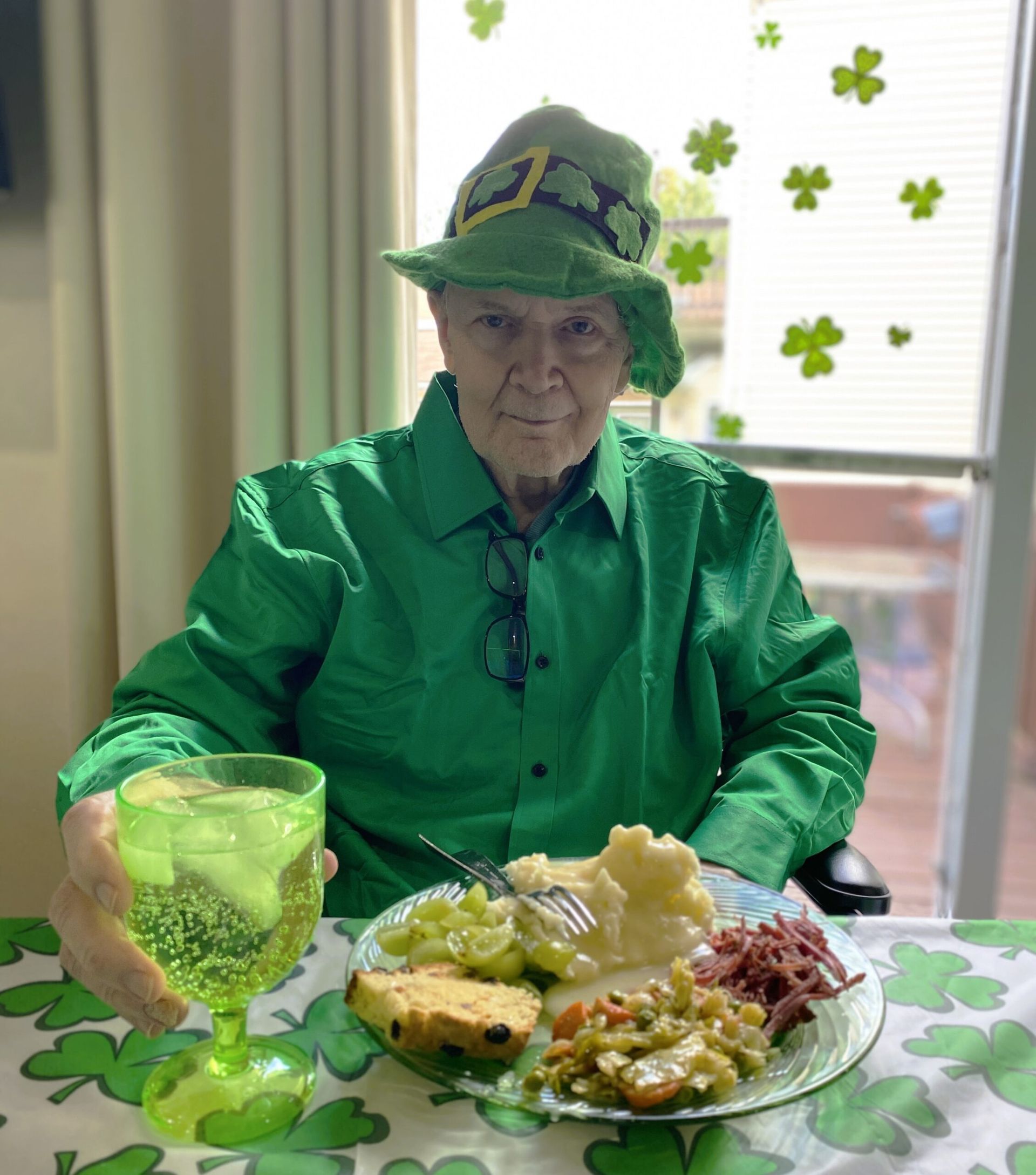 Person in green St. Patrick’s outfit seated at a table with festive shamrock decorations and food.
