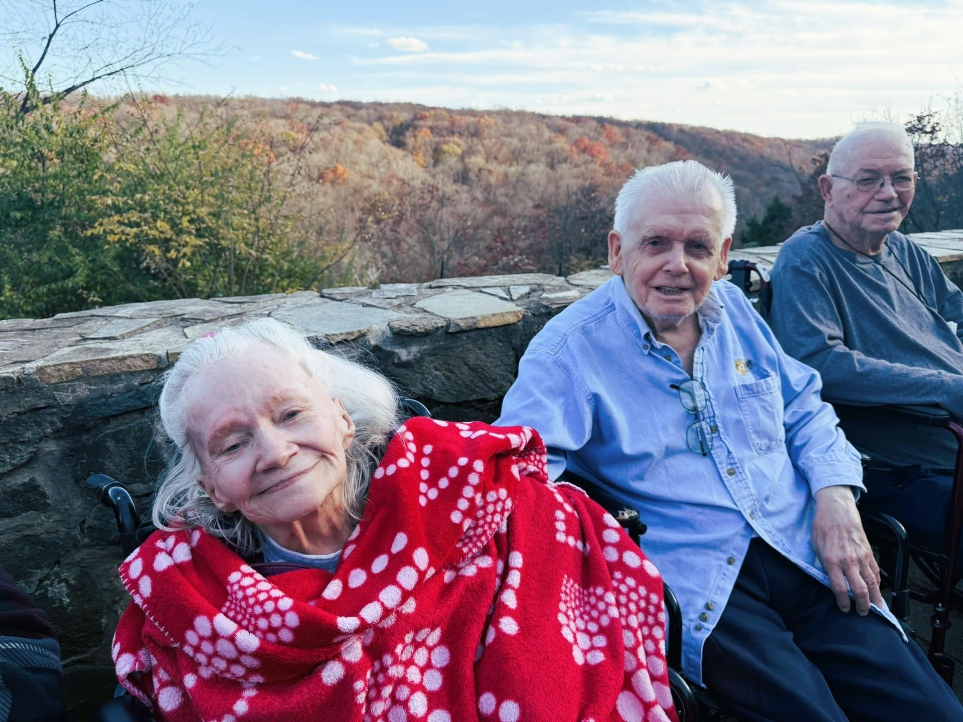 Three people sitting on a stone wall outdoors, with autumn hills in the background.