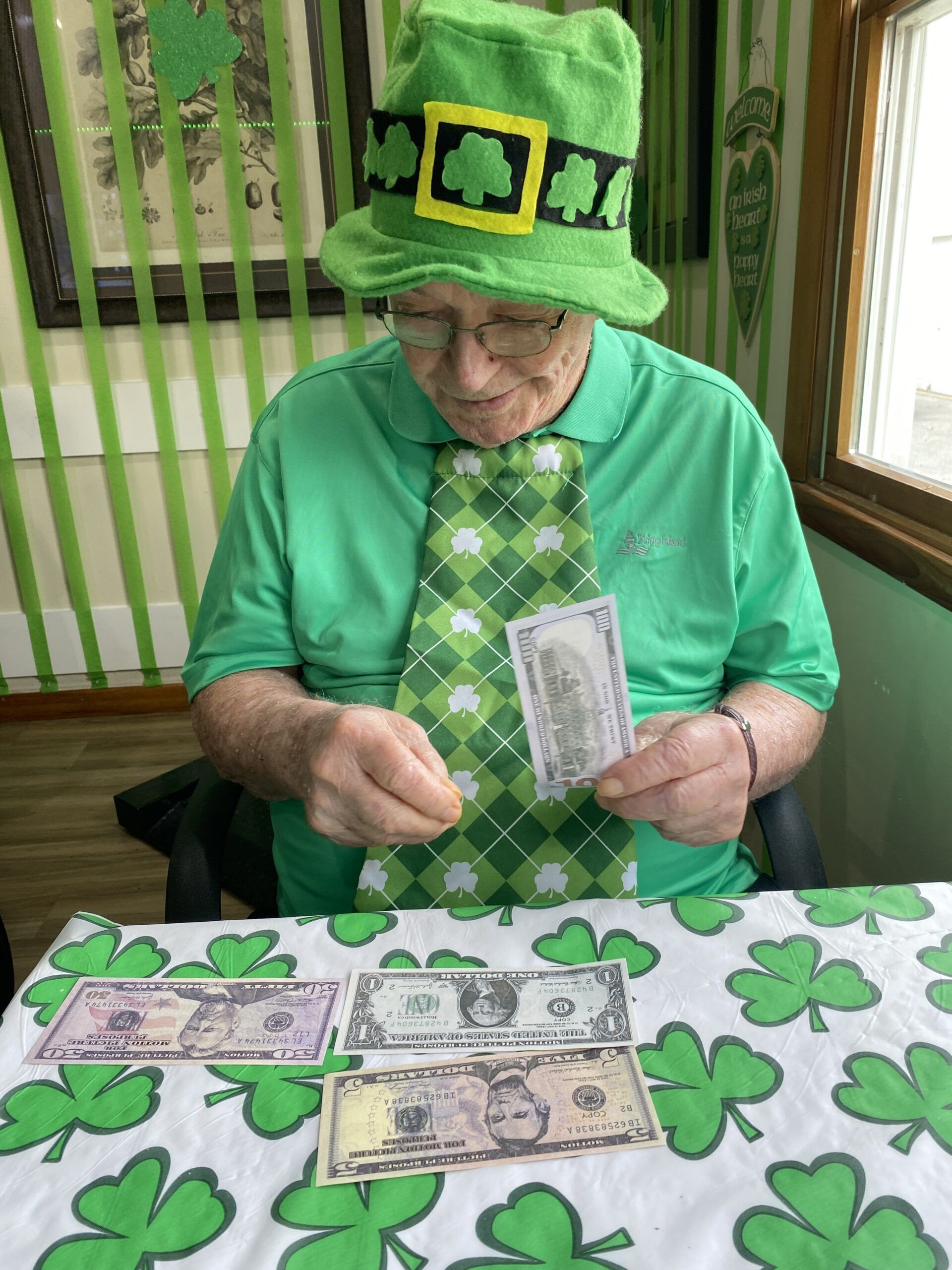 Person in green leprechaun outfit counting cash at a table decorated with shamrocks.