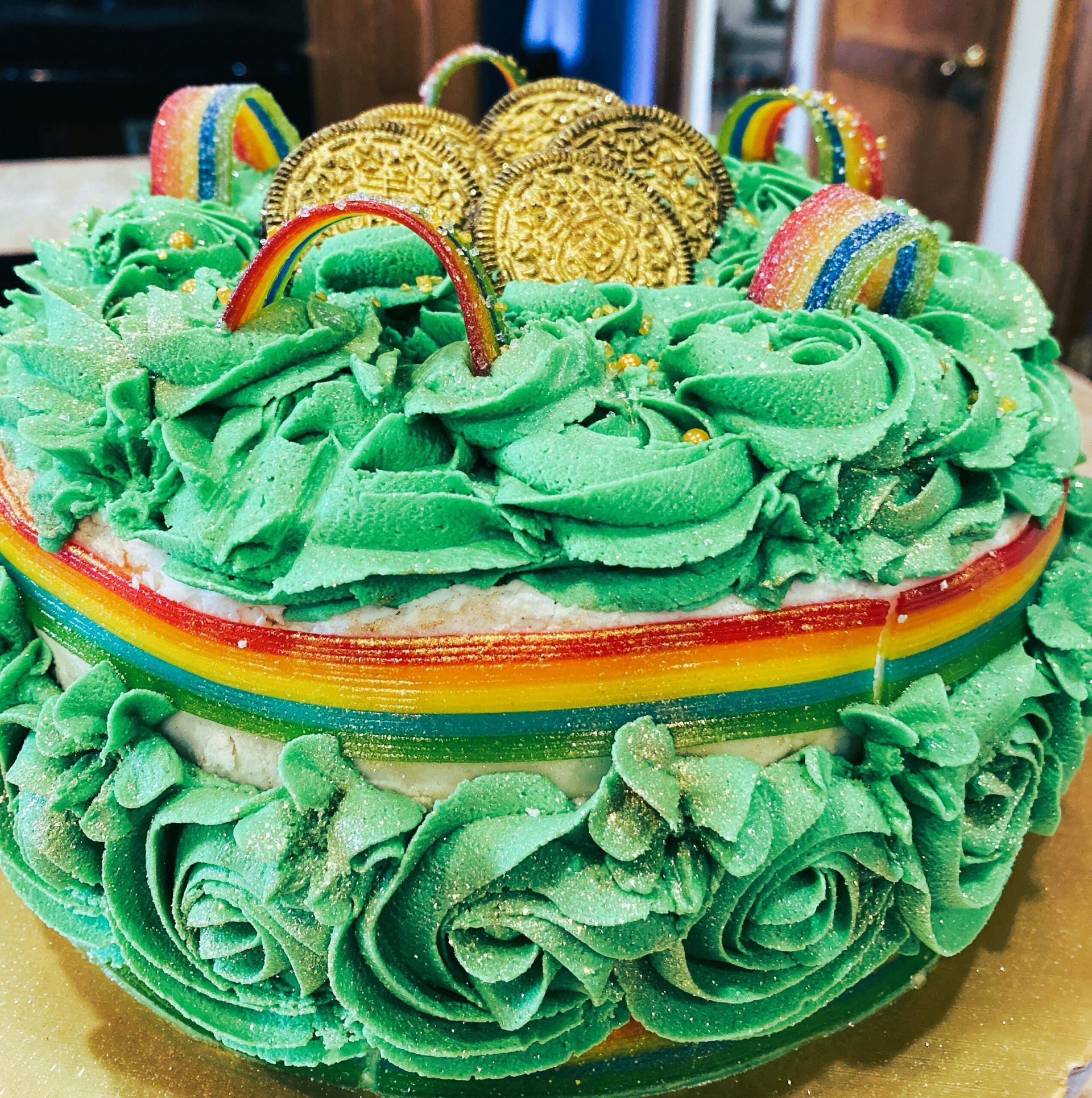 Green-frosted rainbow cake with gold coin toppers and rainbow decorations