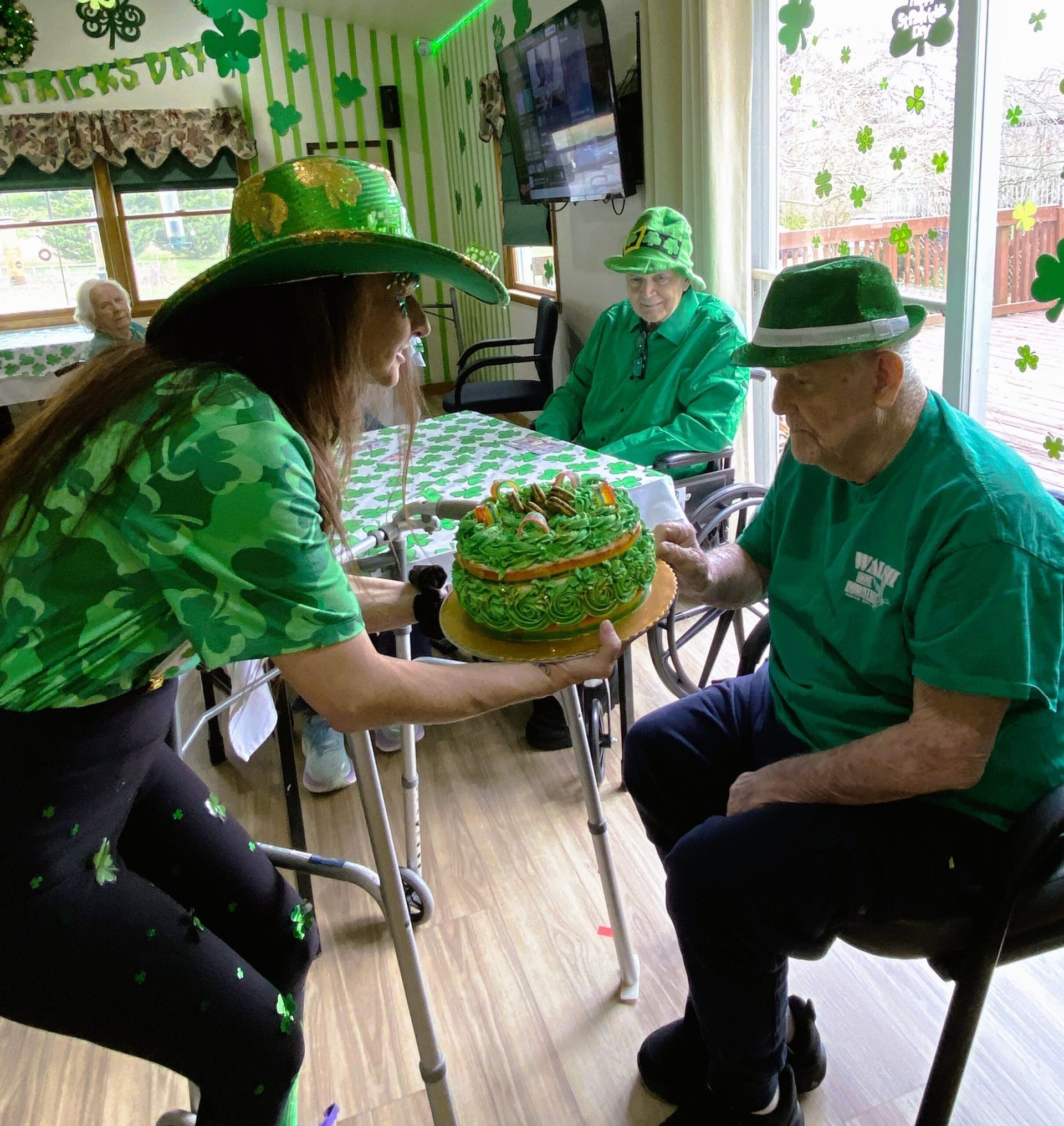 People in green hats and shirts share a decorated cake in a bright room.