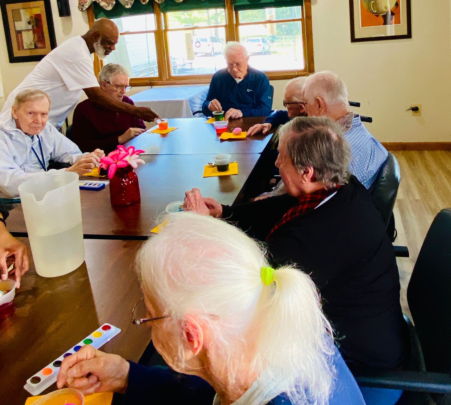People gathered around a table painting small objects in a bright community room