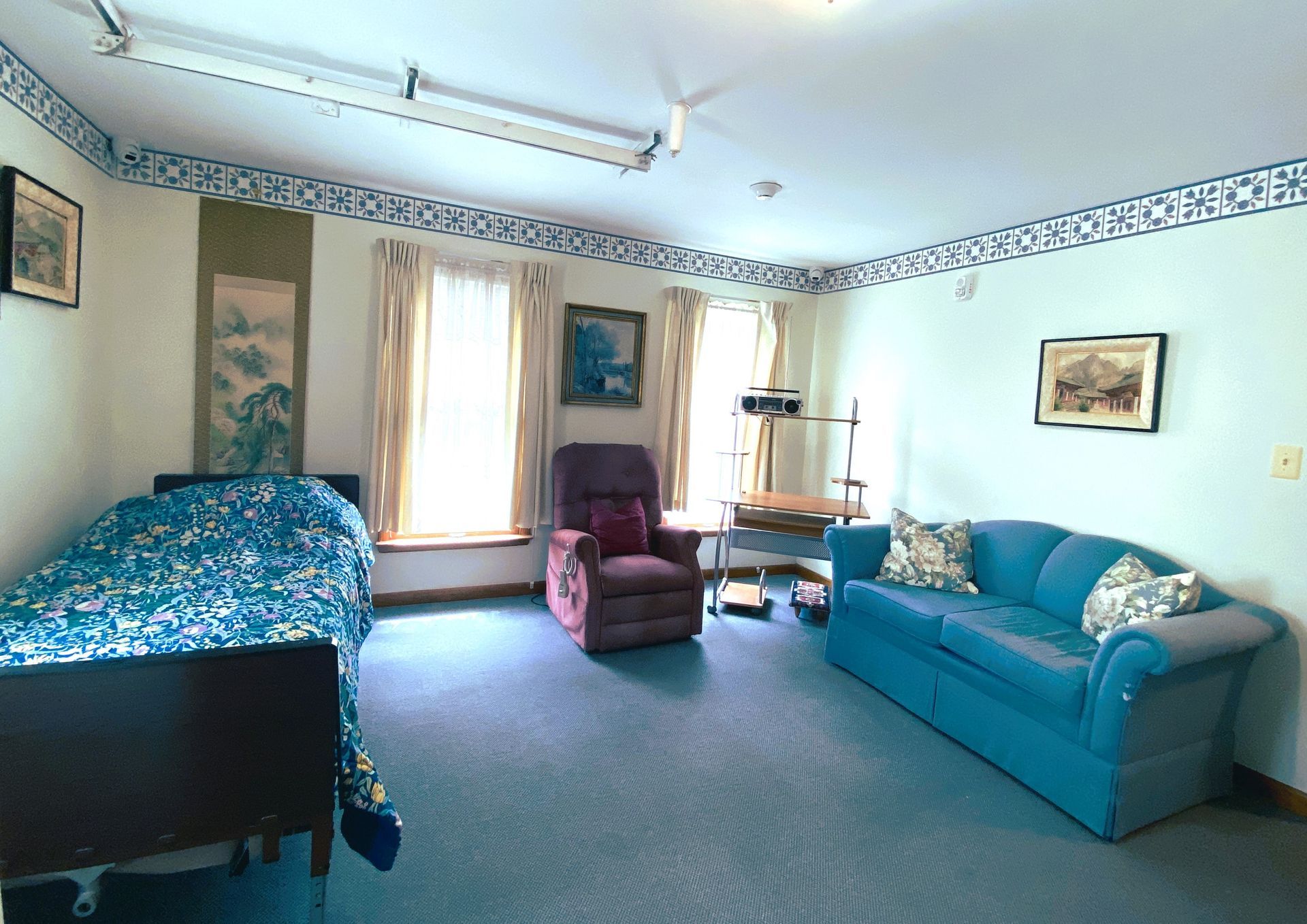 Cozy bedroom with a blue bed, teal sofa, armchair, and patterned wallpaper