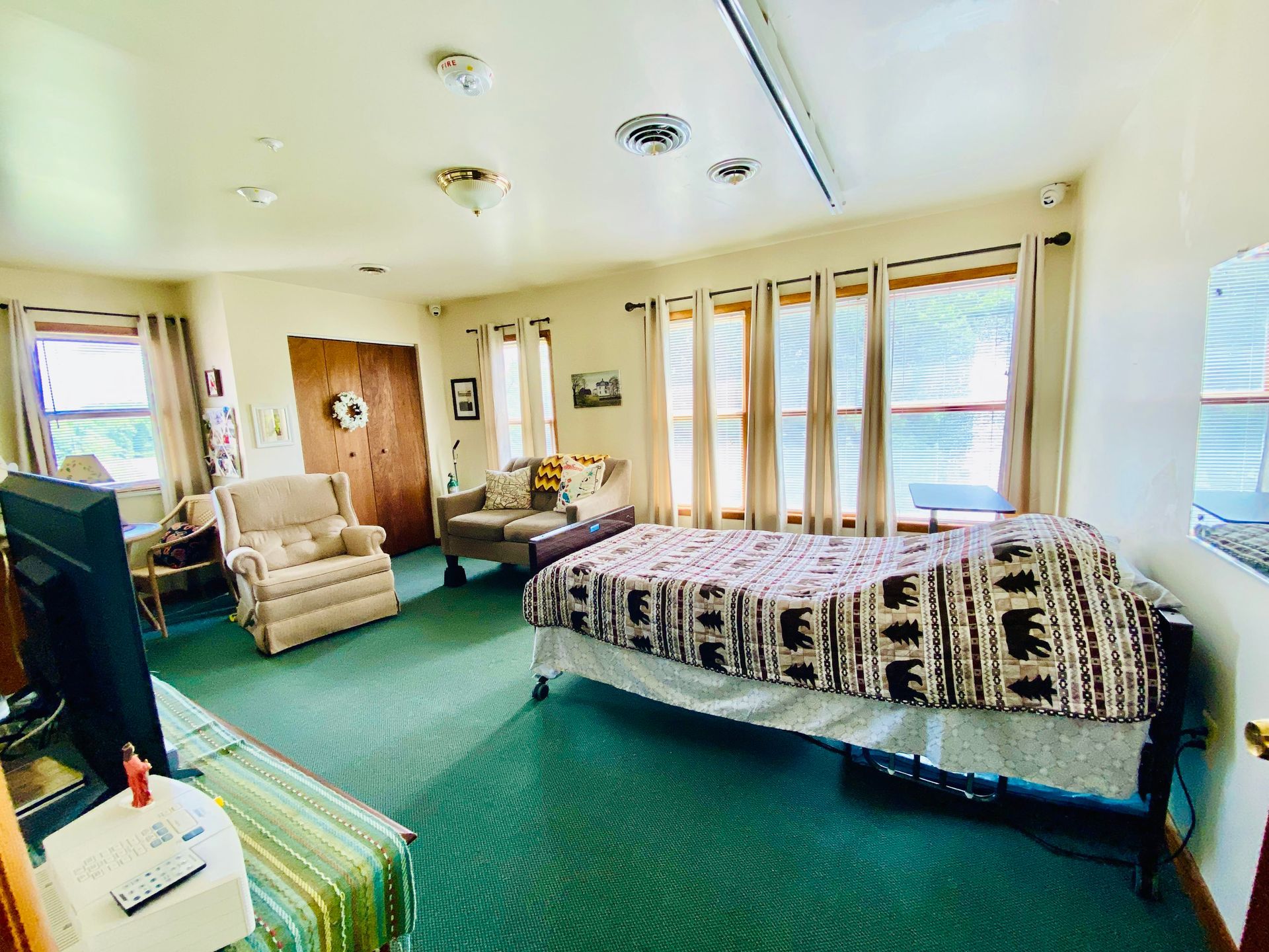 Cozy bedroom with green carpet, two recliners, bed, and large windows with curtains