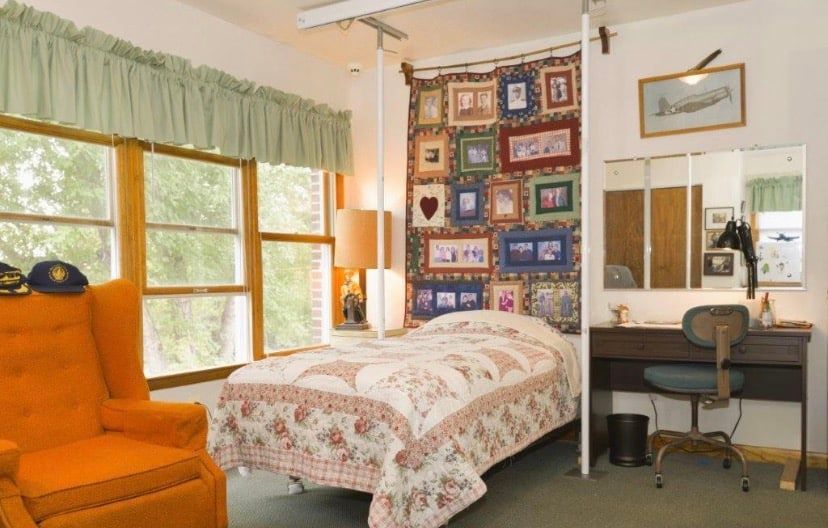 Bright bedroom with orange chair, bed, desk, and colorful quilt wall hanging