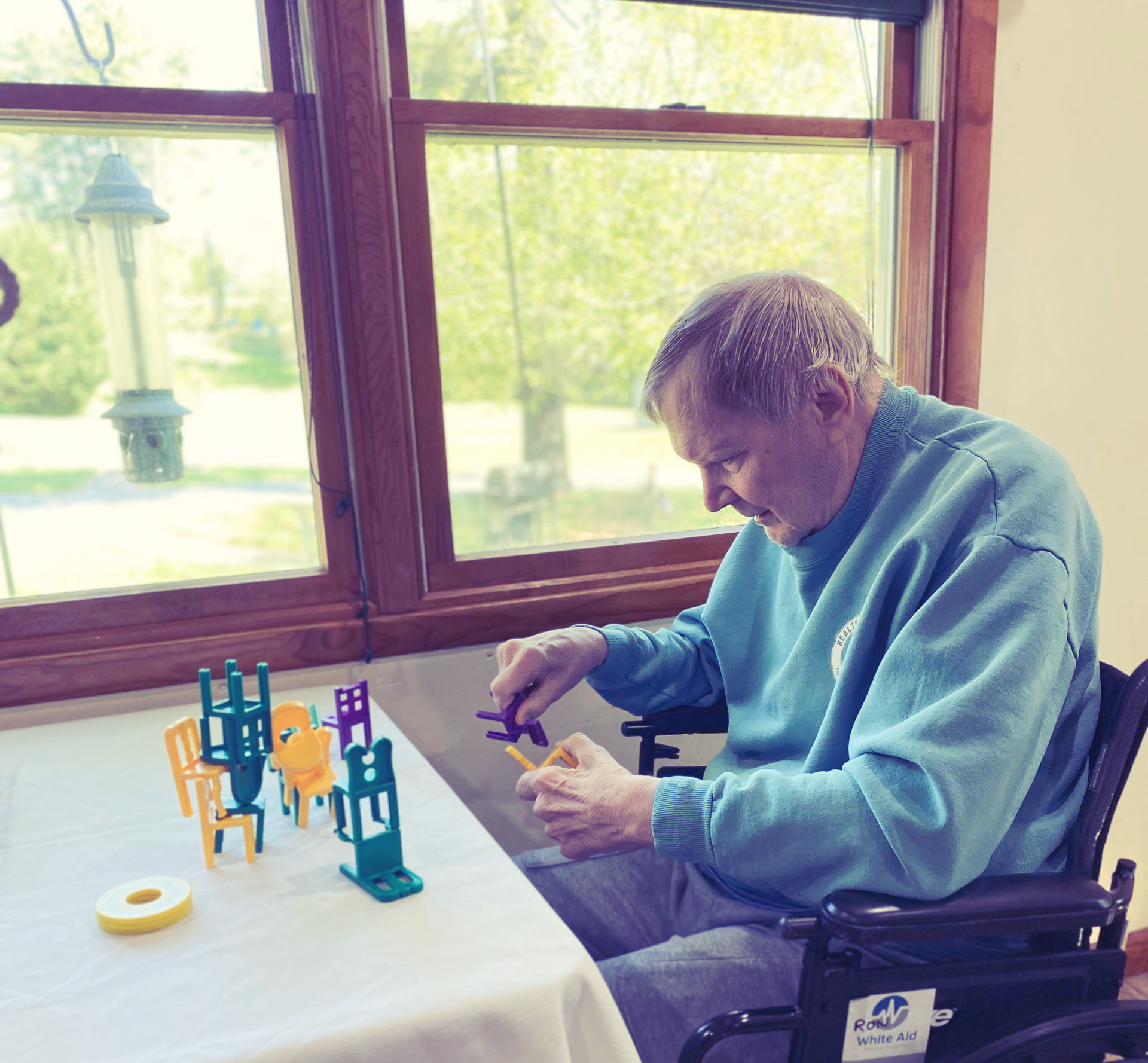 Man seated at a table building a colorful block structure by a window