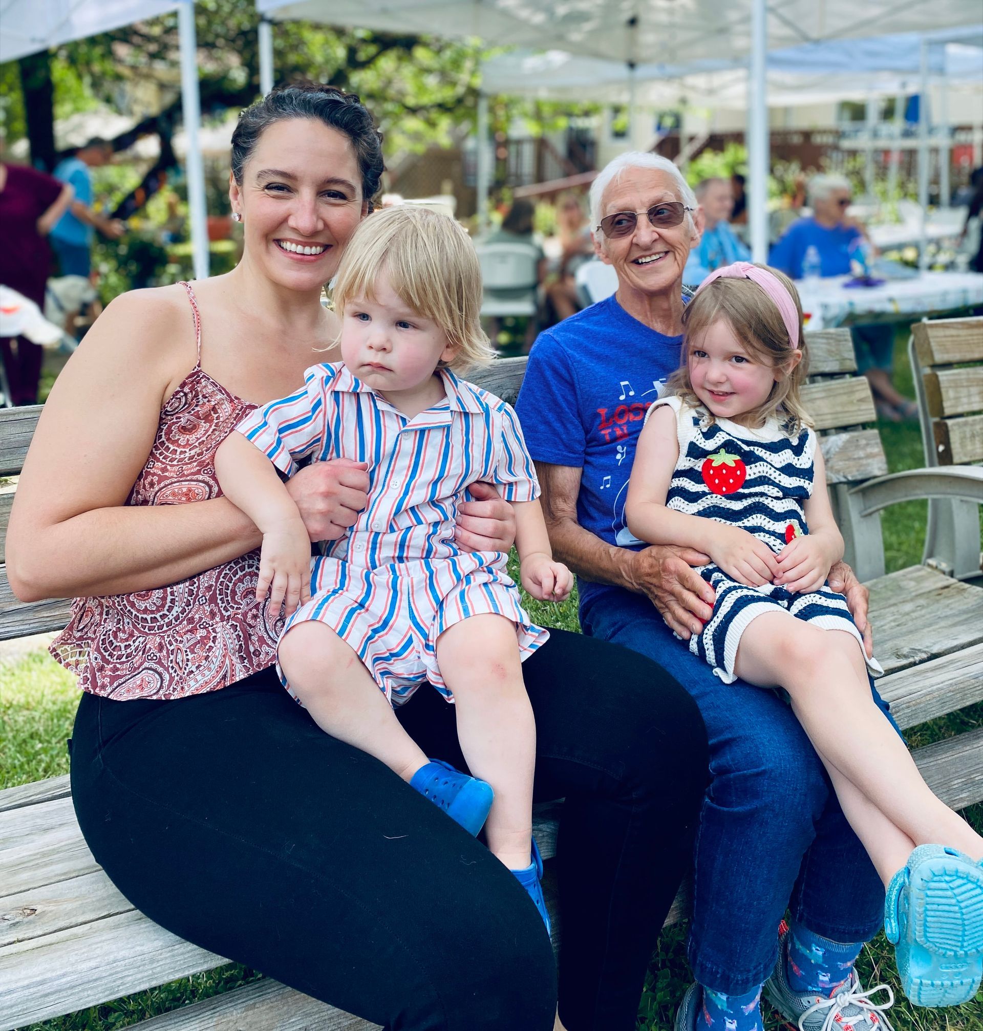 Three people and two children sitting together on a bench outdoors, smiling at a park.