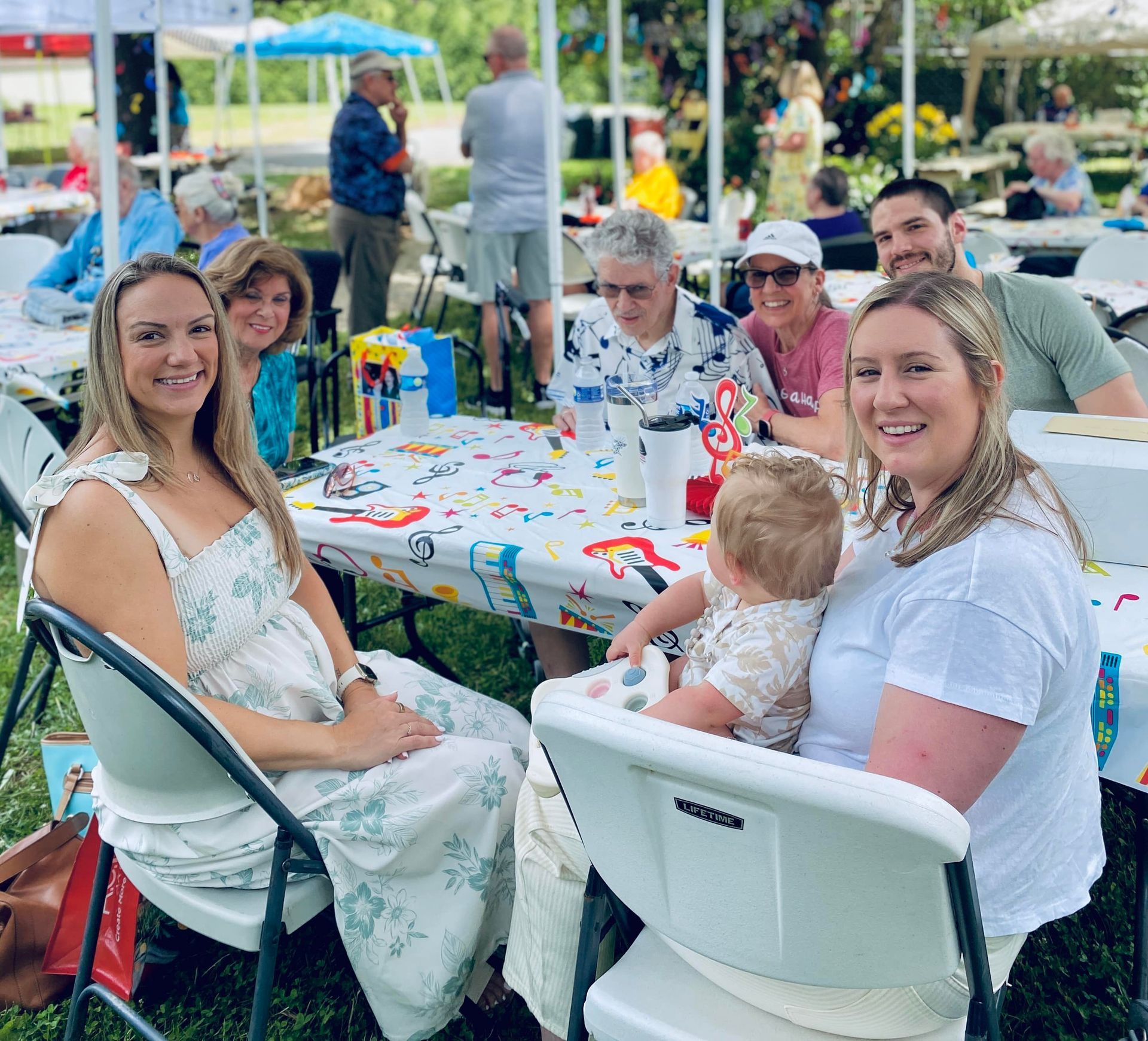 People seated at an outdoor picnic table decorated with colorful confetti, smiling at the camera.