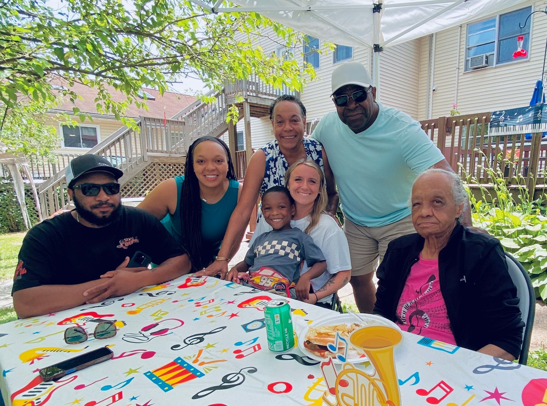 Group gathered around a decorated table under a white outdoor canopy, smiling at a family celebration