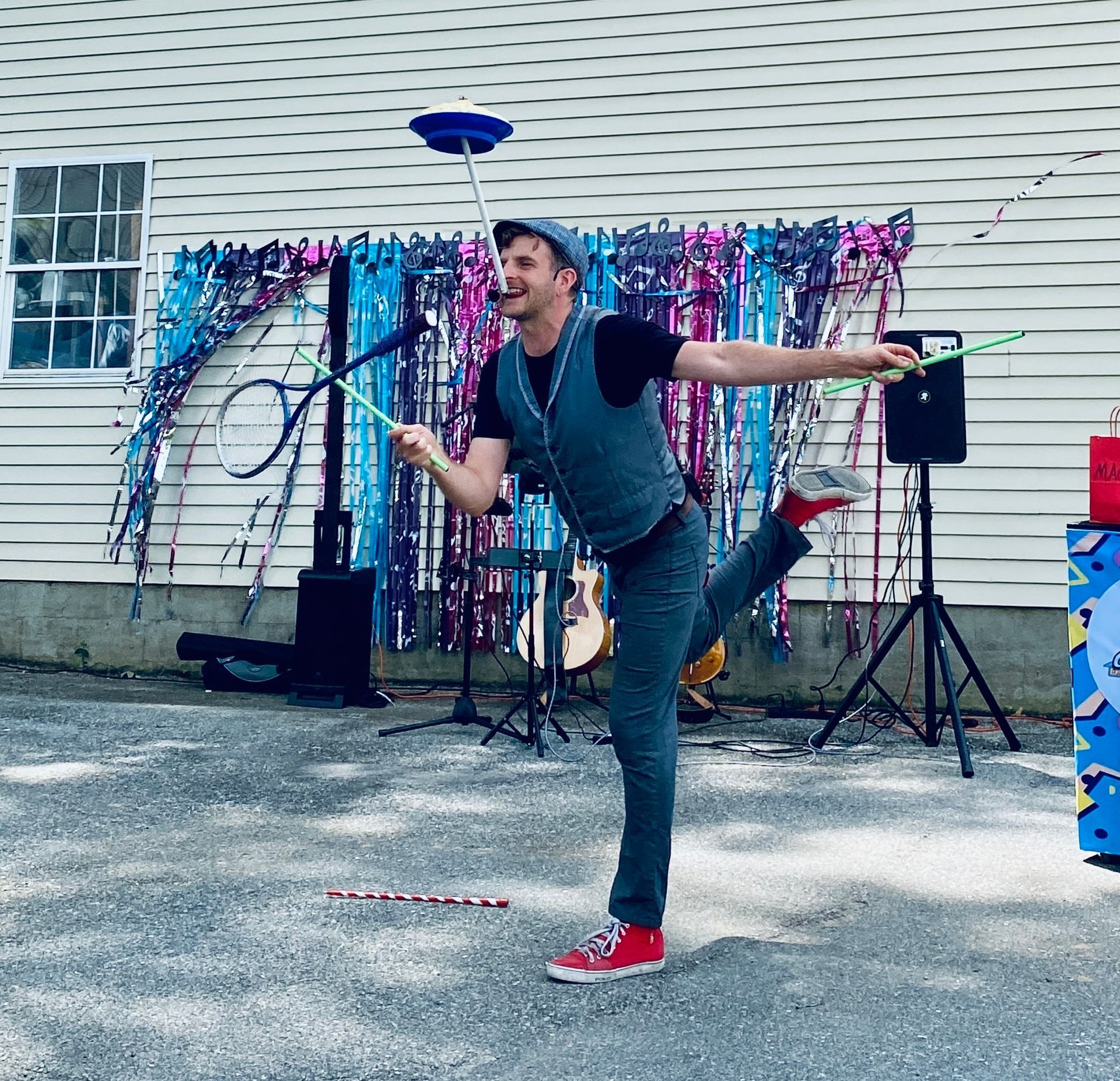 Performer balancing a plate on a stick during an outdoor show before a colorful tinsel backdrop