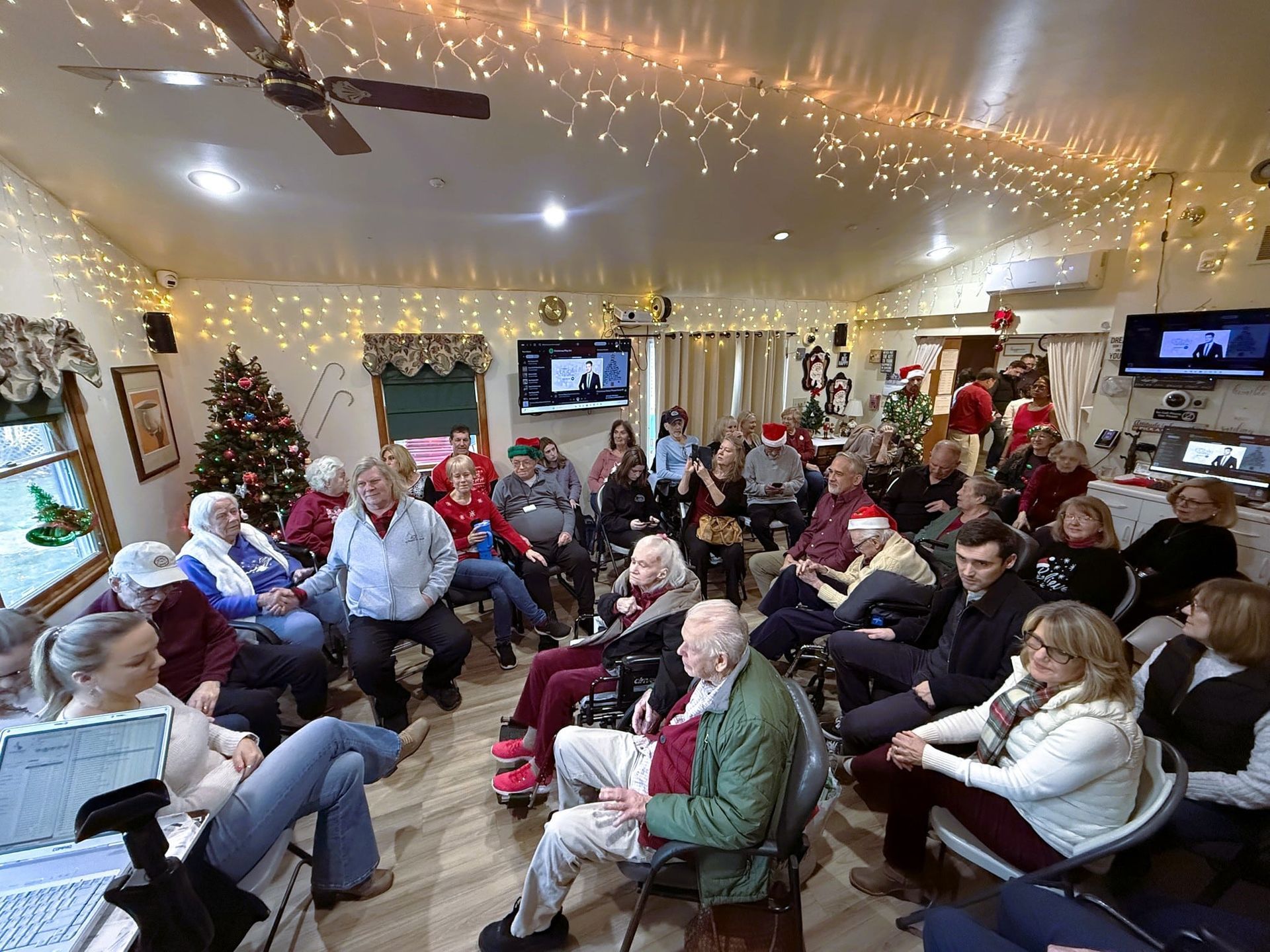 Large group seated in a cozy, decorated living room, watching a TV during a holiday gathering.