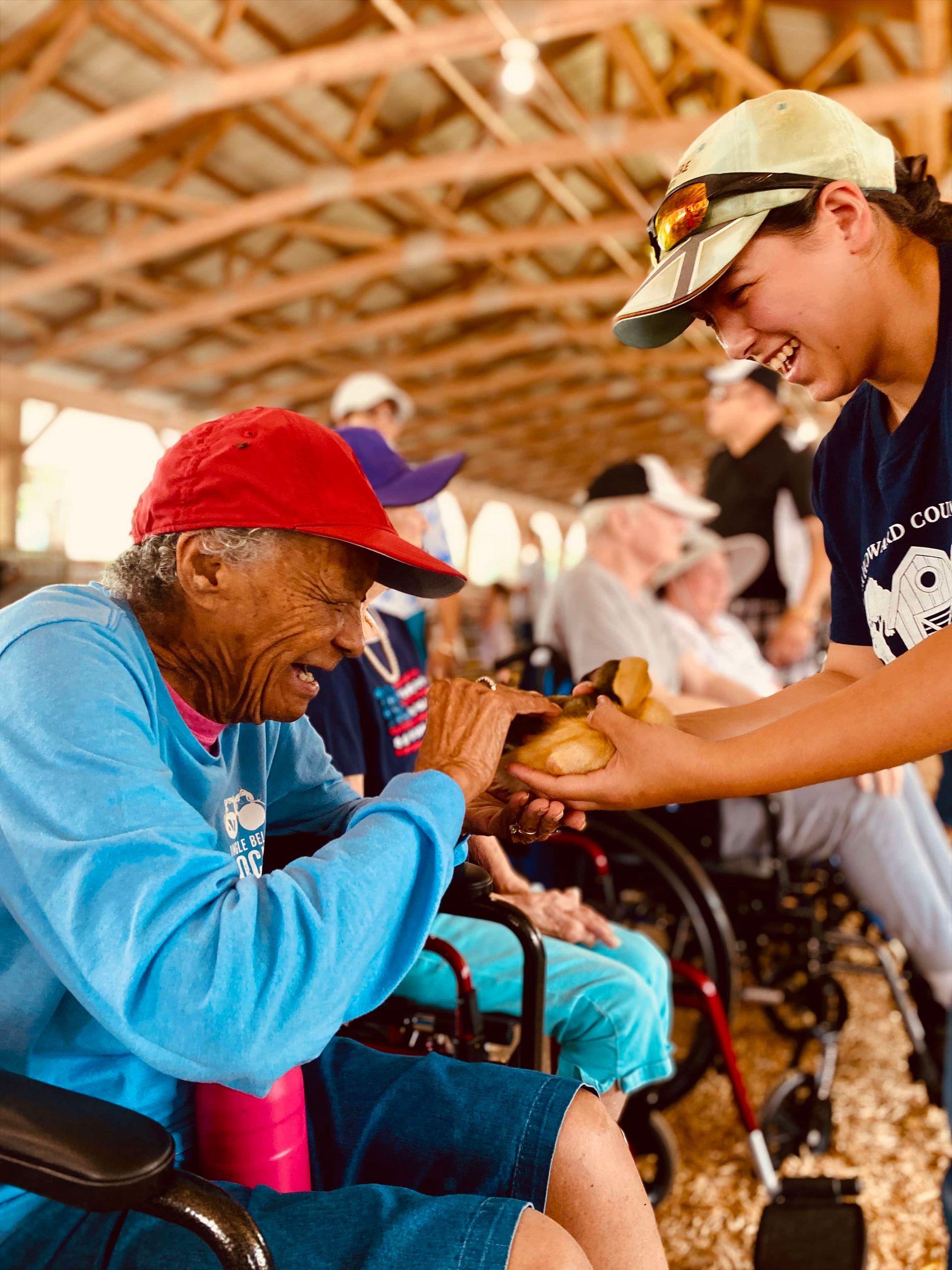 Volunteer handing food to a seated person in a pavilion, with others waiting nearby