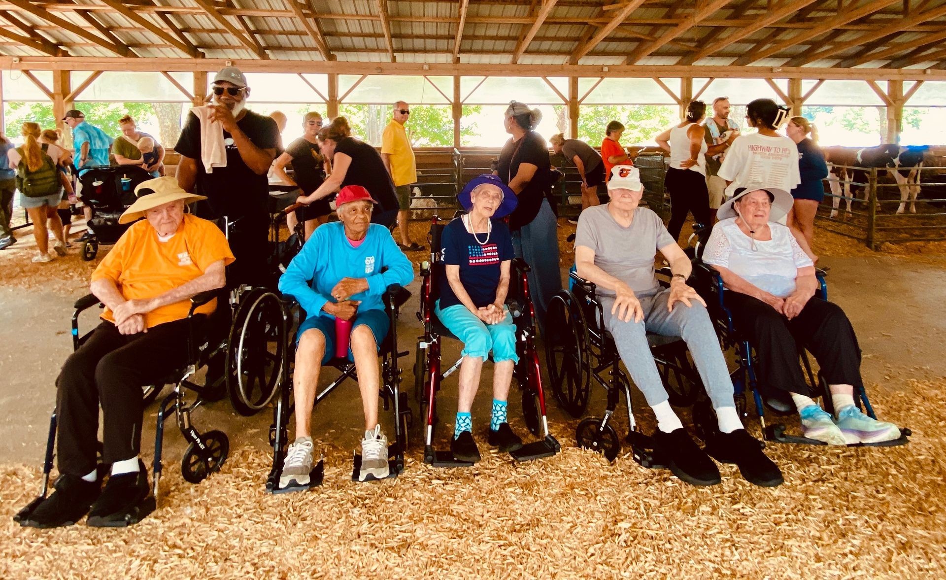 Group seated in a wooden pavilion, many in wheelchairs, posing together in bright sunlight.