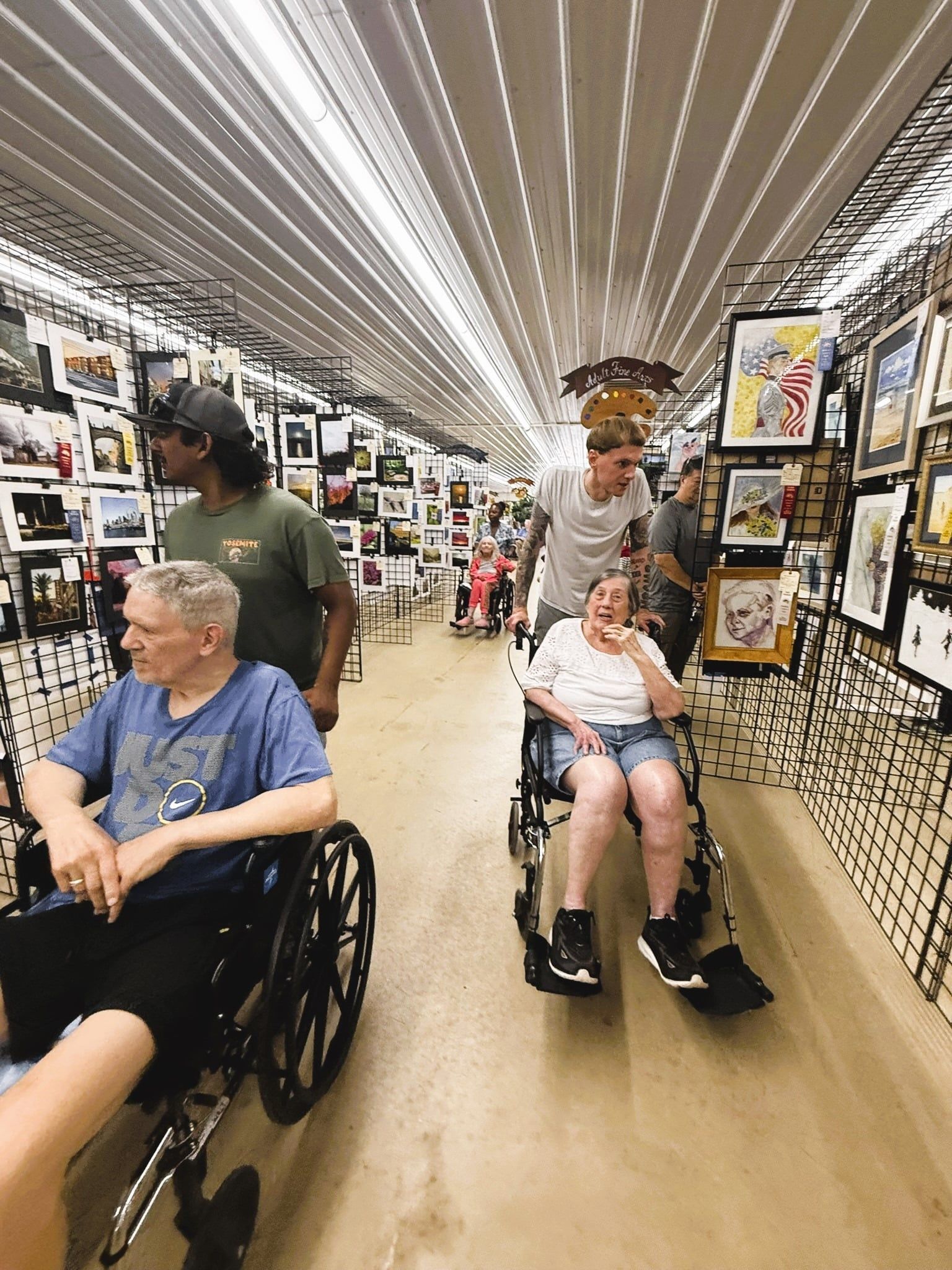 People in wheelchairs browsing framed art in a bright gallery aisle