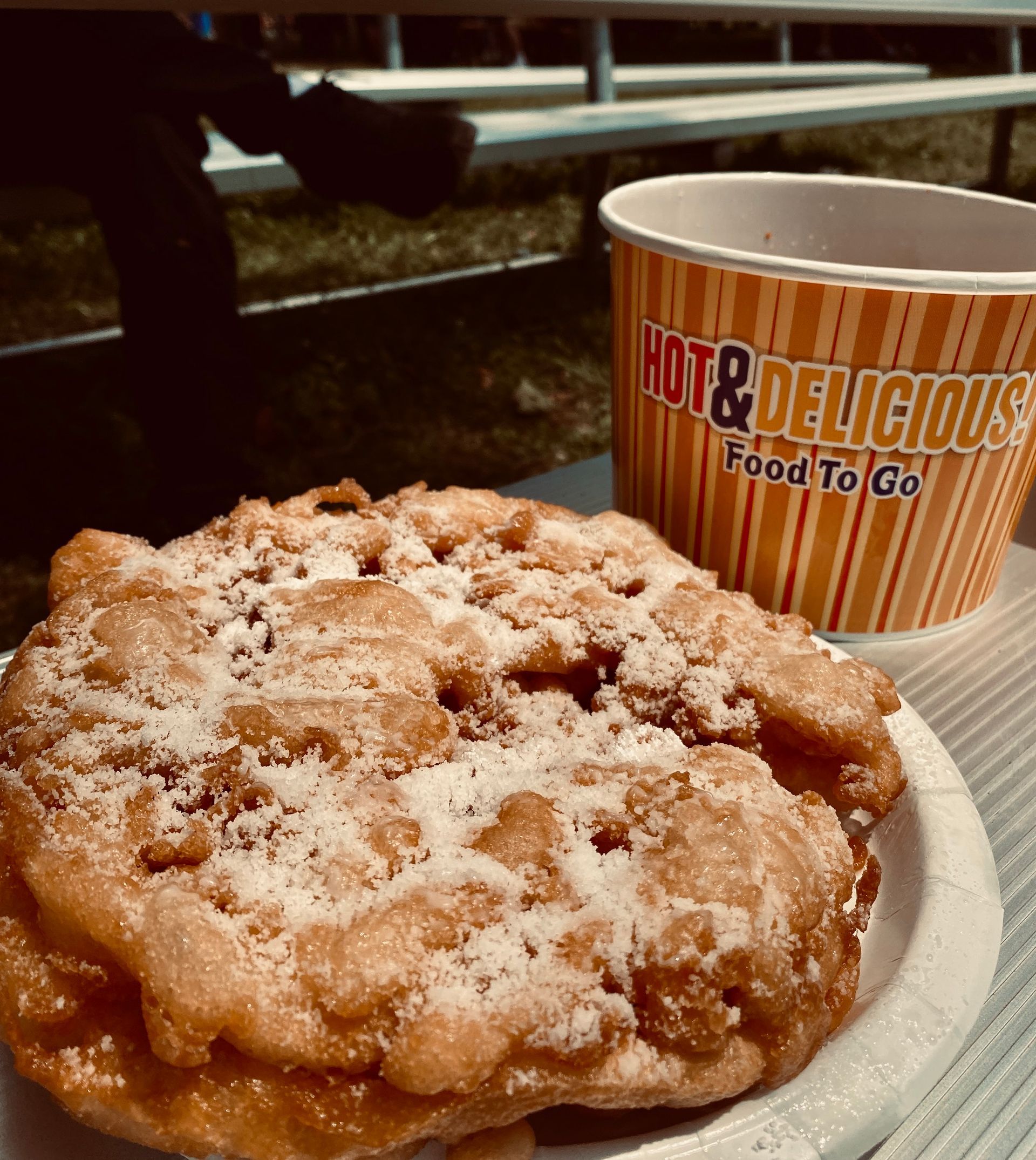 Powdered funnel cake on a plate beside a Hot & Delicious Food To Go cup