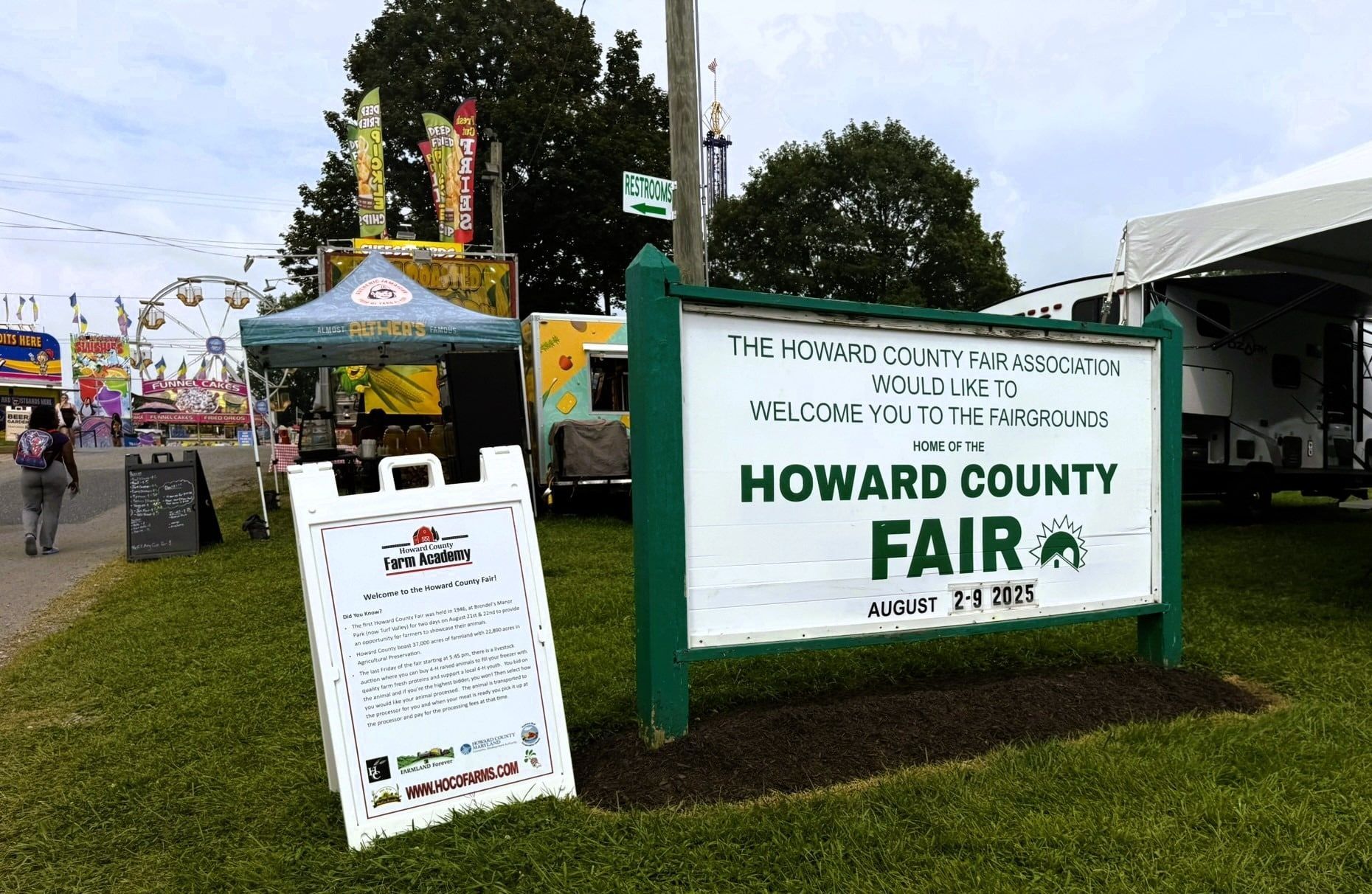 Howard County Fair entrance sign beside a green tent and event kiosk on a grassy fairground
