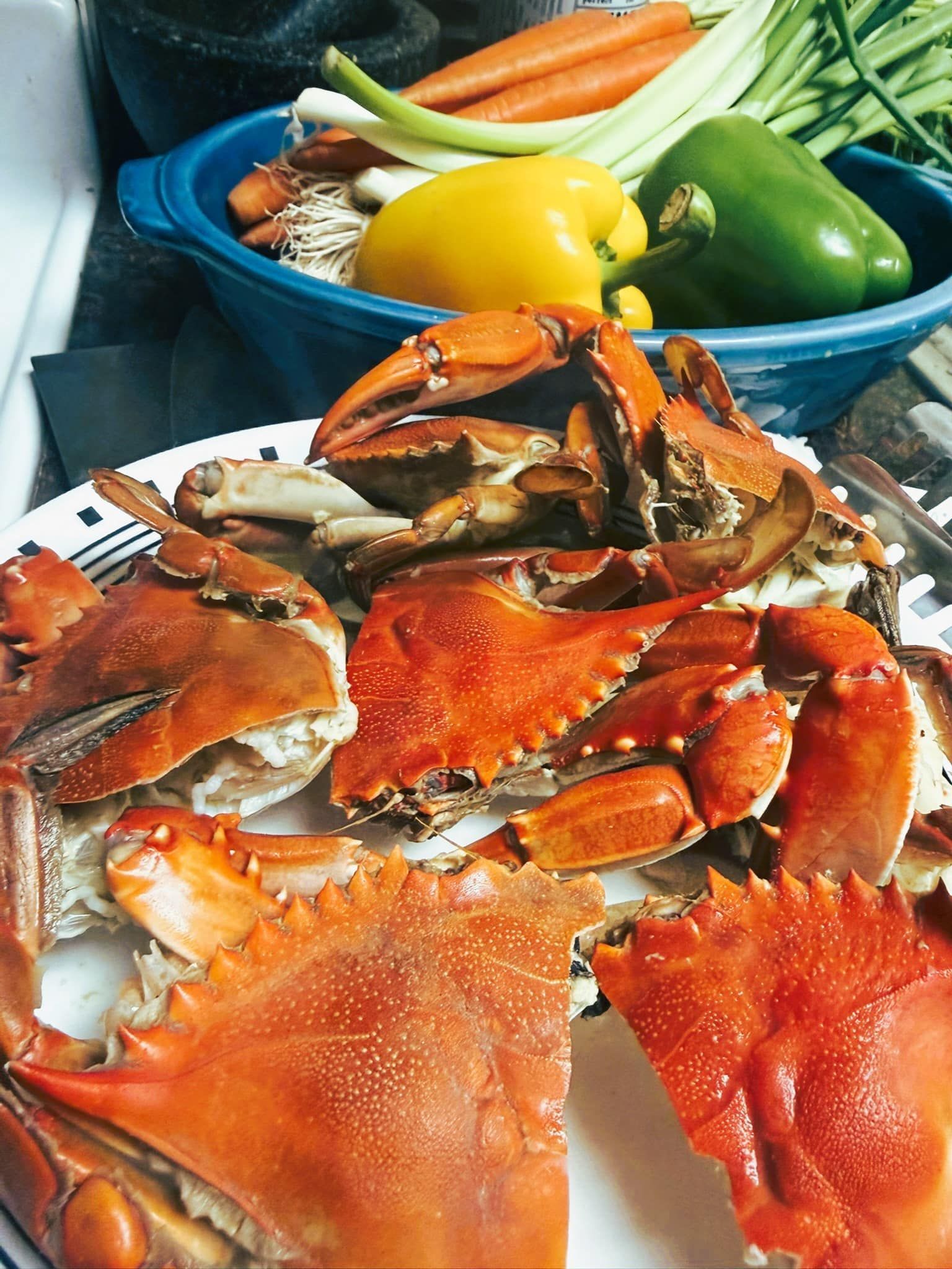 Crab shells on a plate beside a blue bowl of fresh vegetables, including peppers and carrots.