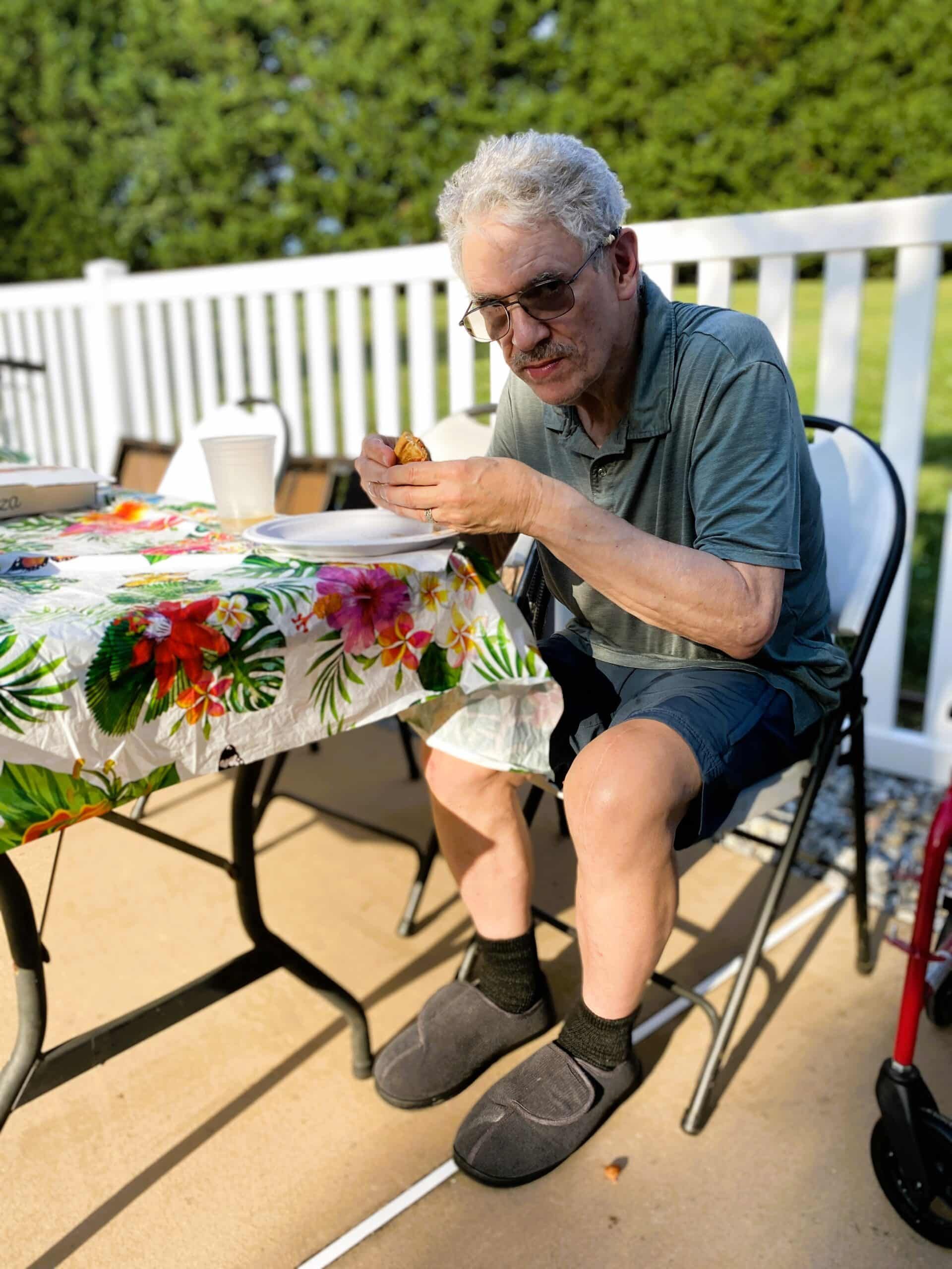 Man sitting outdoors at a table, eating from a bowl on a sunny patio.