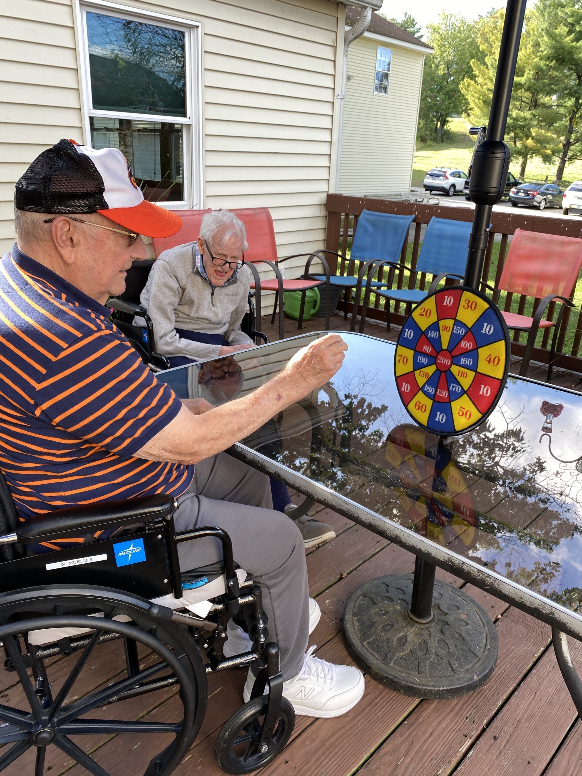 Man in wheelchair at outdoor patio game, aiming at colorful spinner beside seated companion