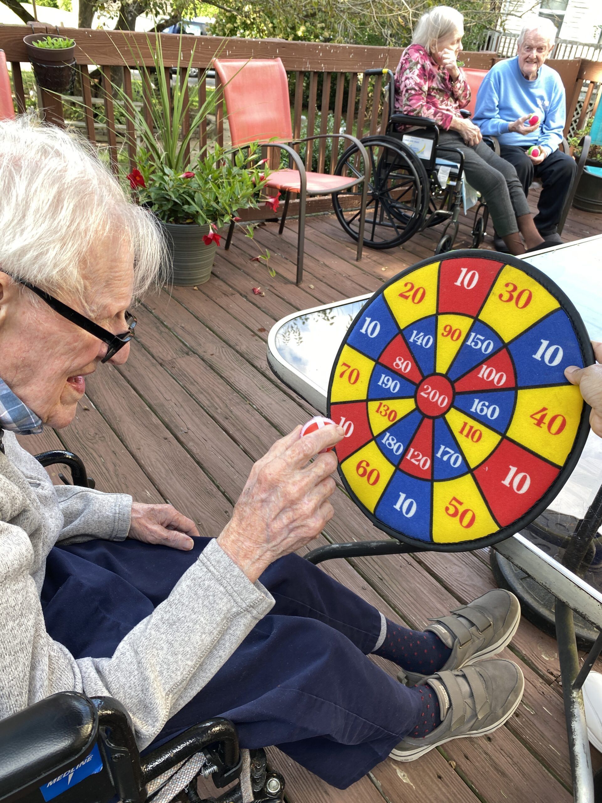 Person in wheelchair aiming at colorful numbered game wheel on a wooden deck with seated people nearby