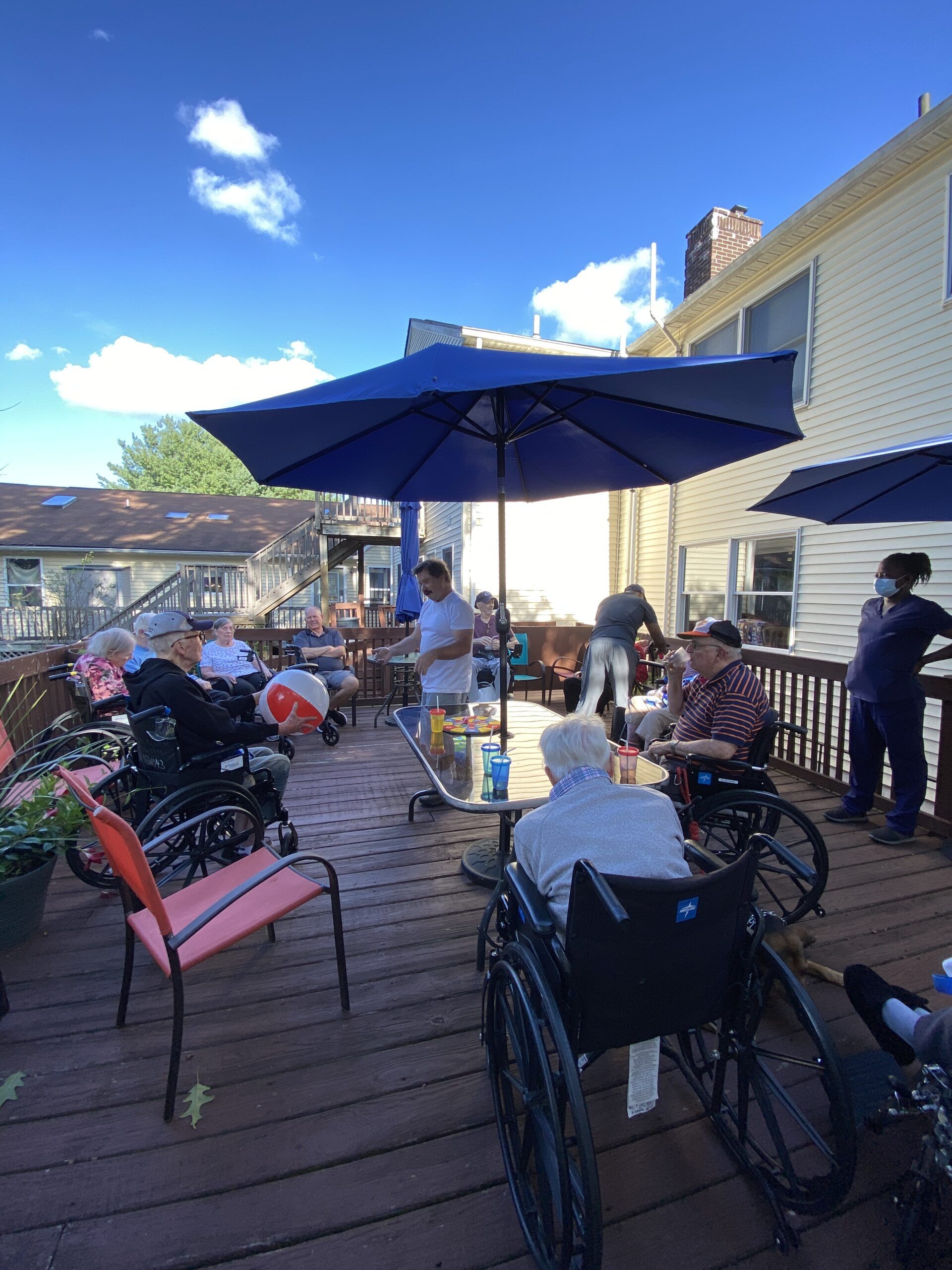 People sitting on a sunny wooden patio under blue umbrellas, with bicycles nearby.