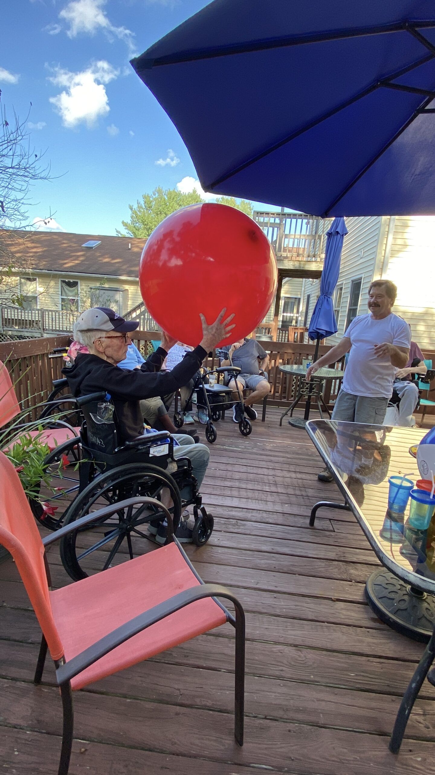 Outdoor café patio with people, a red balloon, bicycles, and a large blue umbrella
