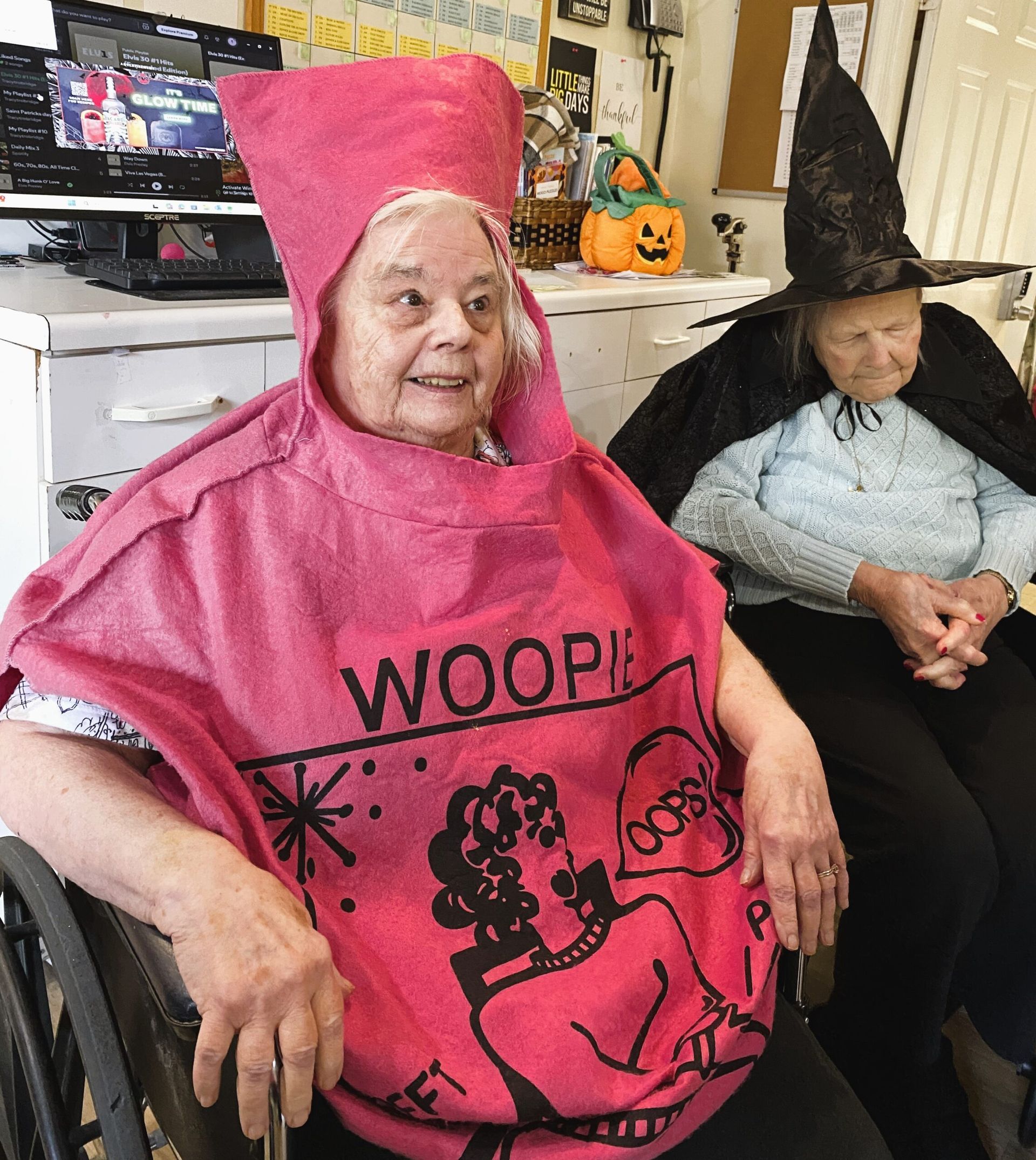 Two people in pink and black Halloween costumes sitting indoors, one smiling in a bright pink outfit.