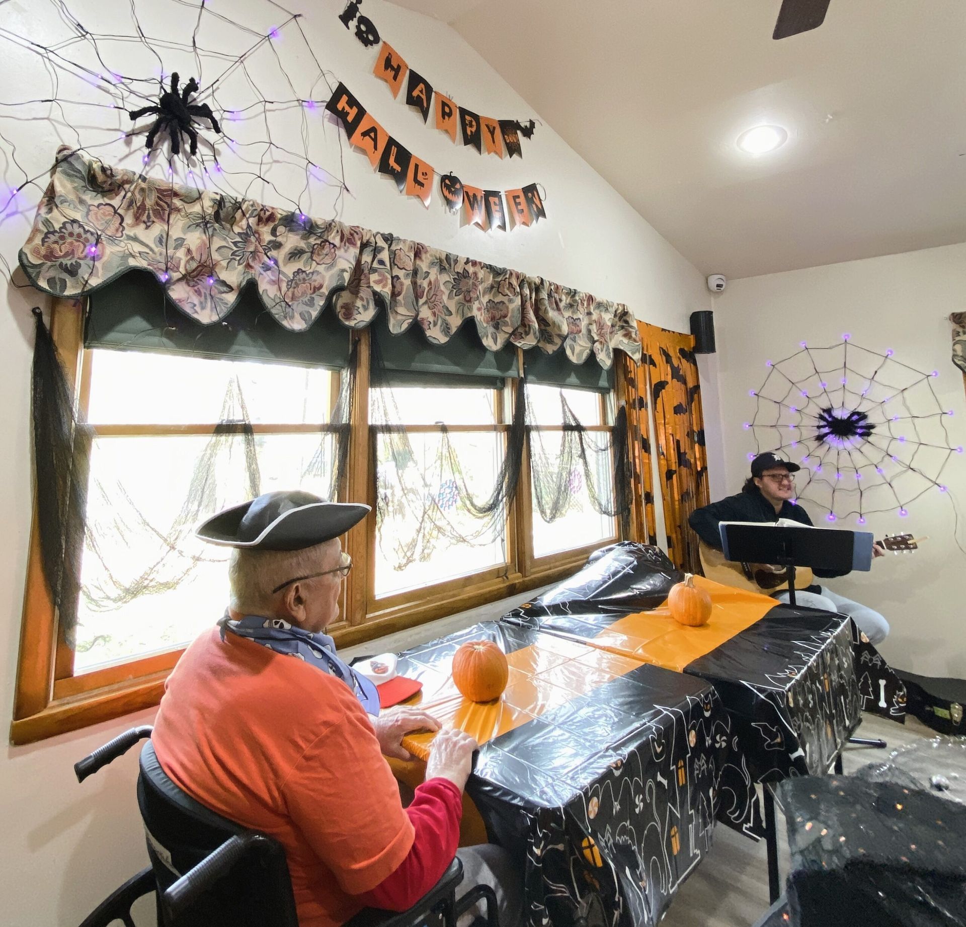 Two costumed people in a Halloween-decorated room with spider webs, pumpkins, and black table coverings