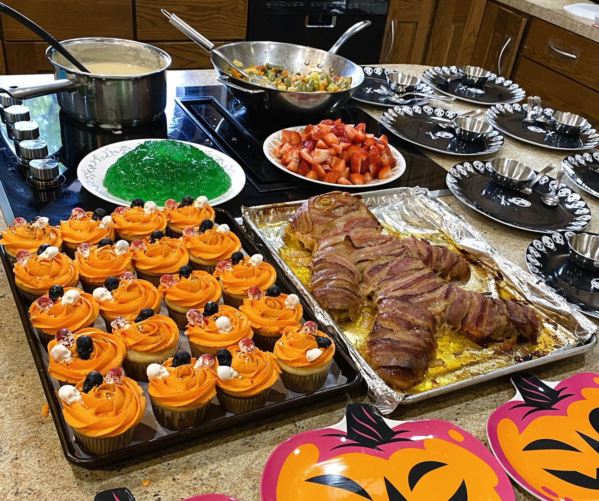 Buffet table with roast meat, orange frosted cupcakes, green gelatin, and trays of assorted desserts