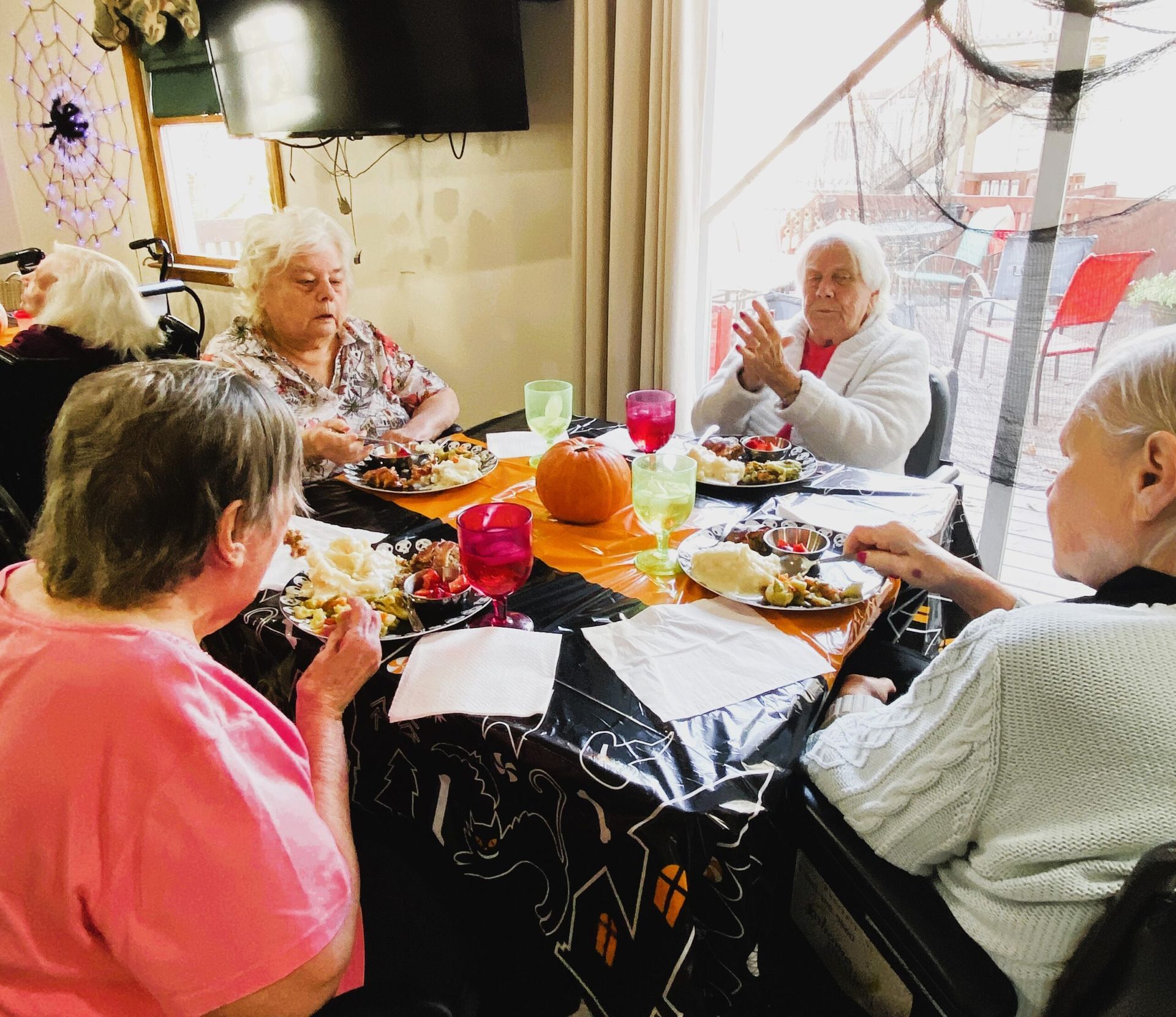 Four people sit around a table with food and gifts, chatting in a cozy room.