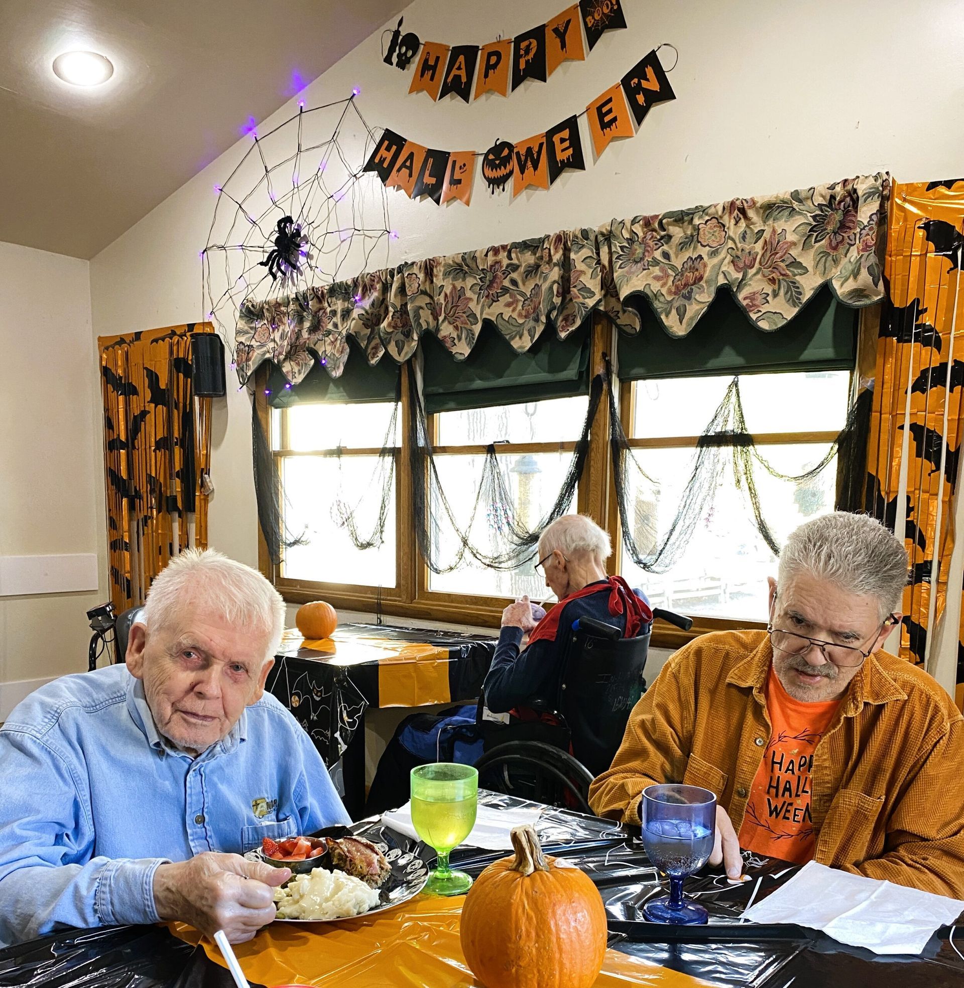 Three people at a Halloween-decorated dining table with a pumpkin centerpiece