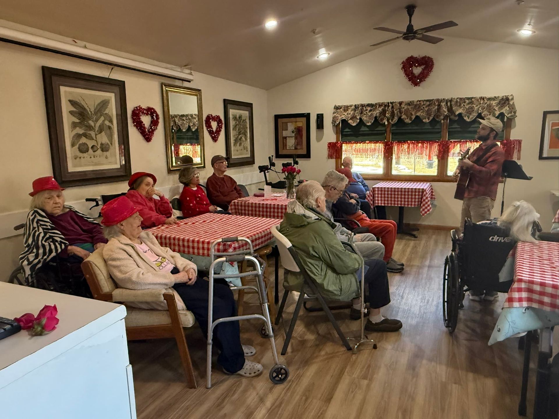 People seated in a cozy room with red-and-white checkered decor, listening to a speaker near the window.