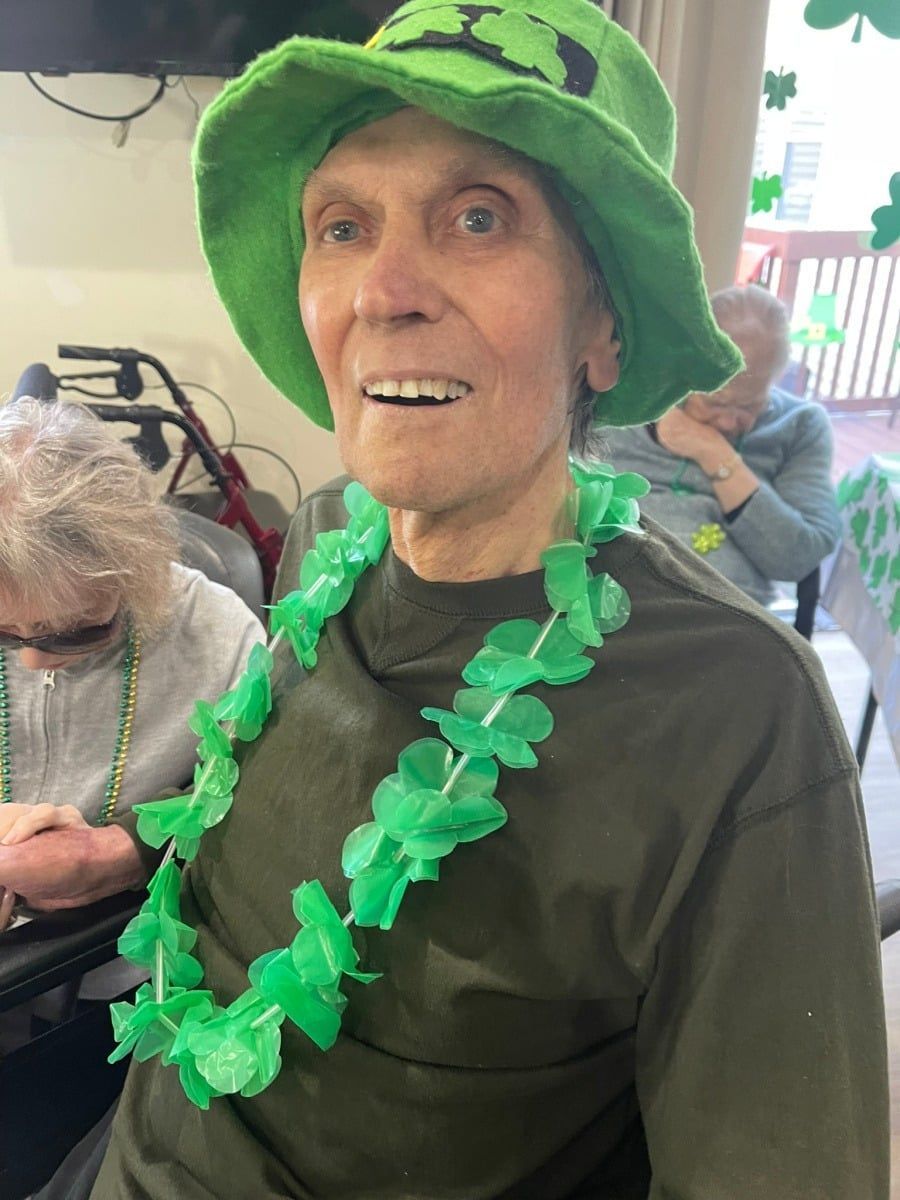 Person in a bright green hat and lei, smiling while seated indoors