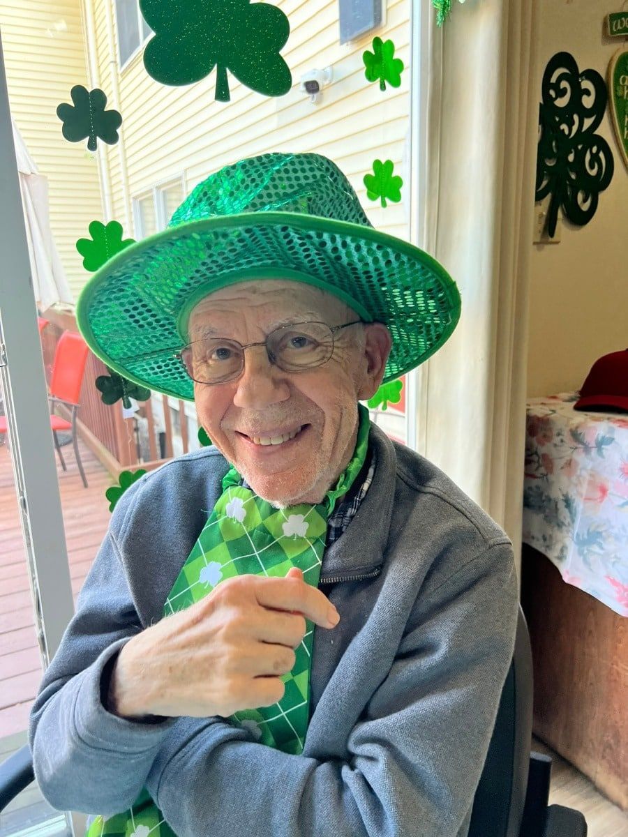 Person in a green hat and shamrock tie smiling indoors with St. Patrick’s Day decorations