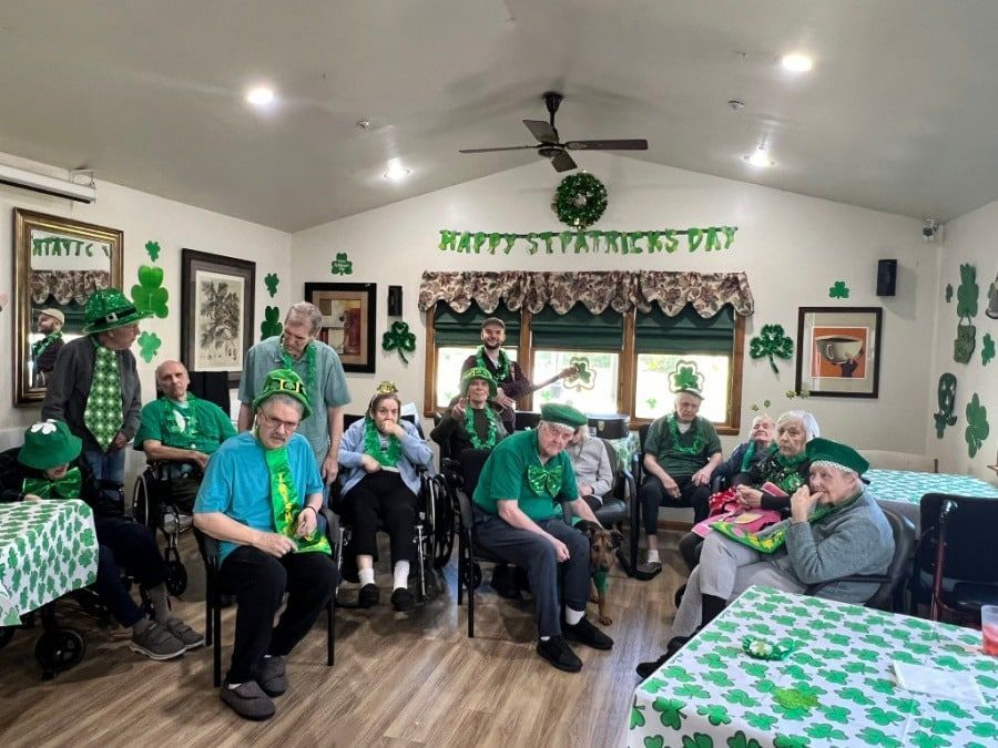 People seated in a green-decorated room, gathered for a festive celebration with tables, banners, and balloons.