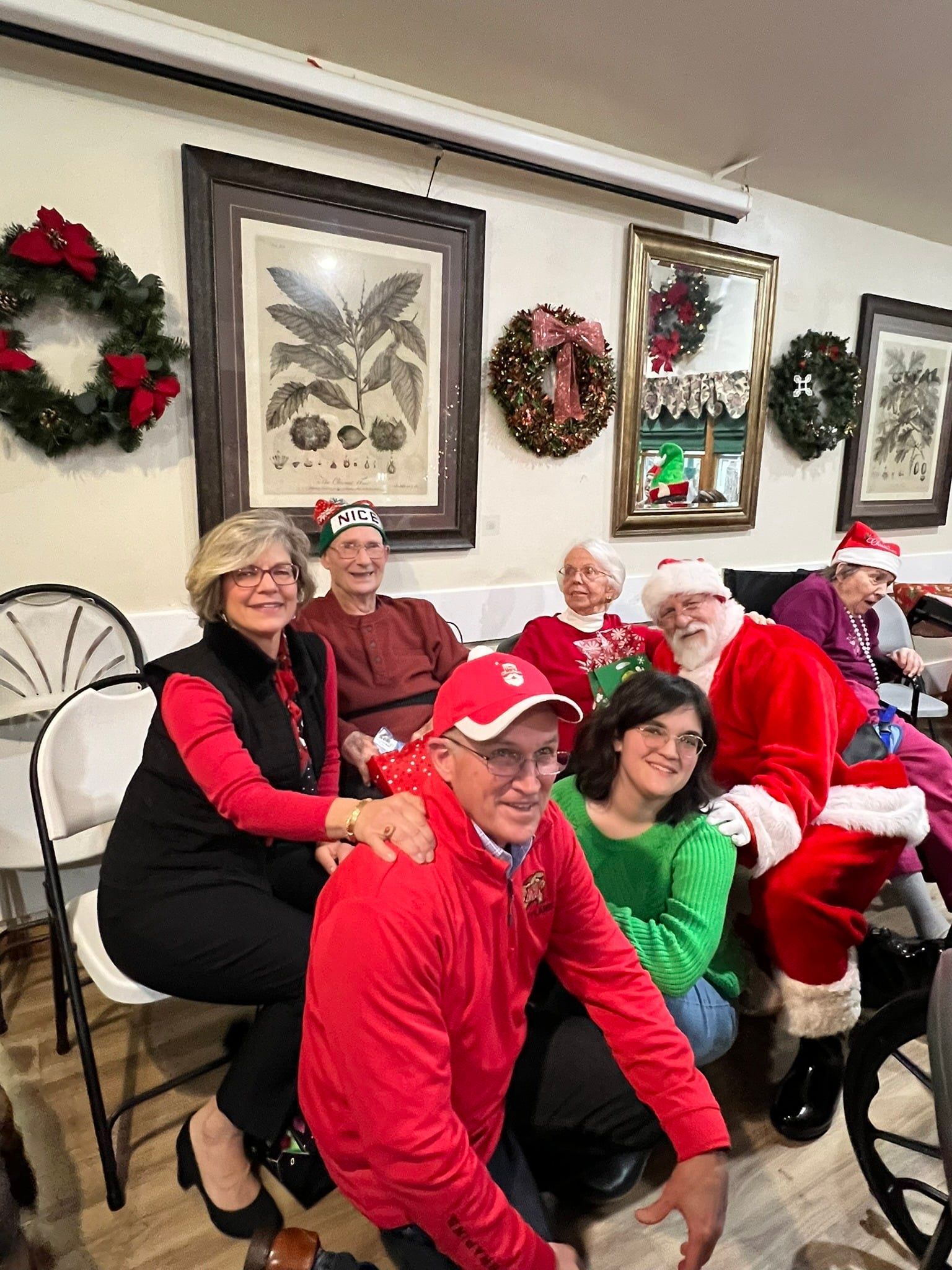 Group in festive holiday outfits seated indoors with wreaths and framed wall art behind them