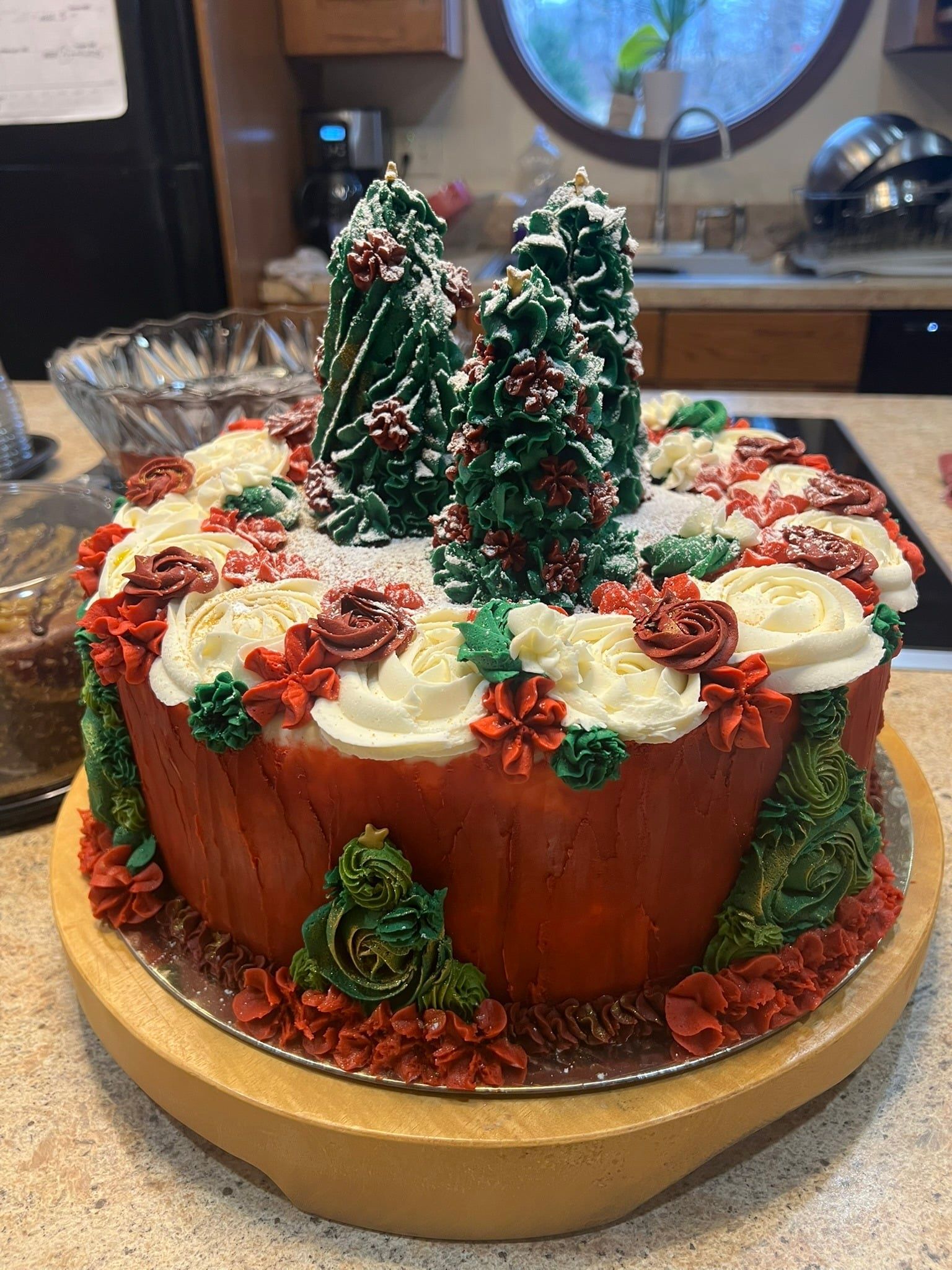 Decorated holiday cake with red and white frosting, green trees, and berries on a gold stand