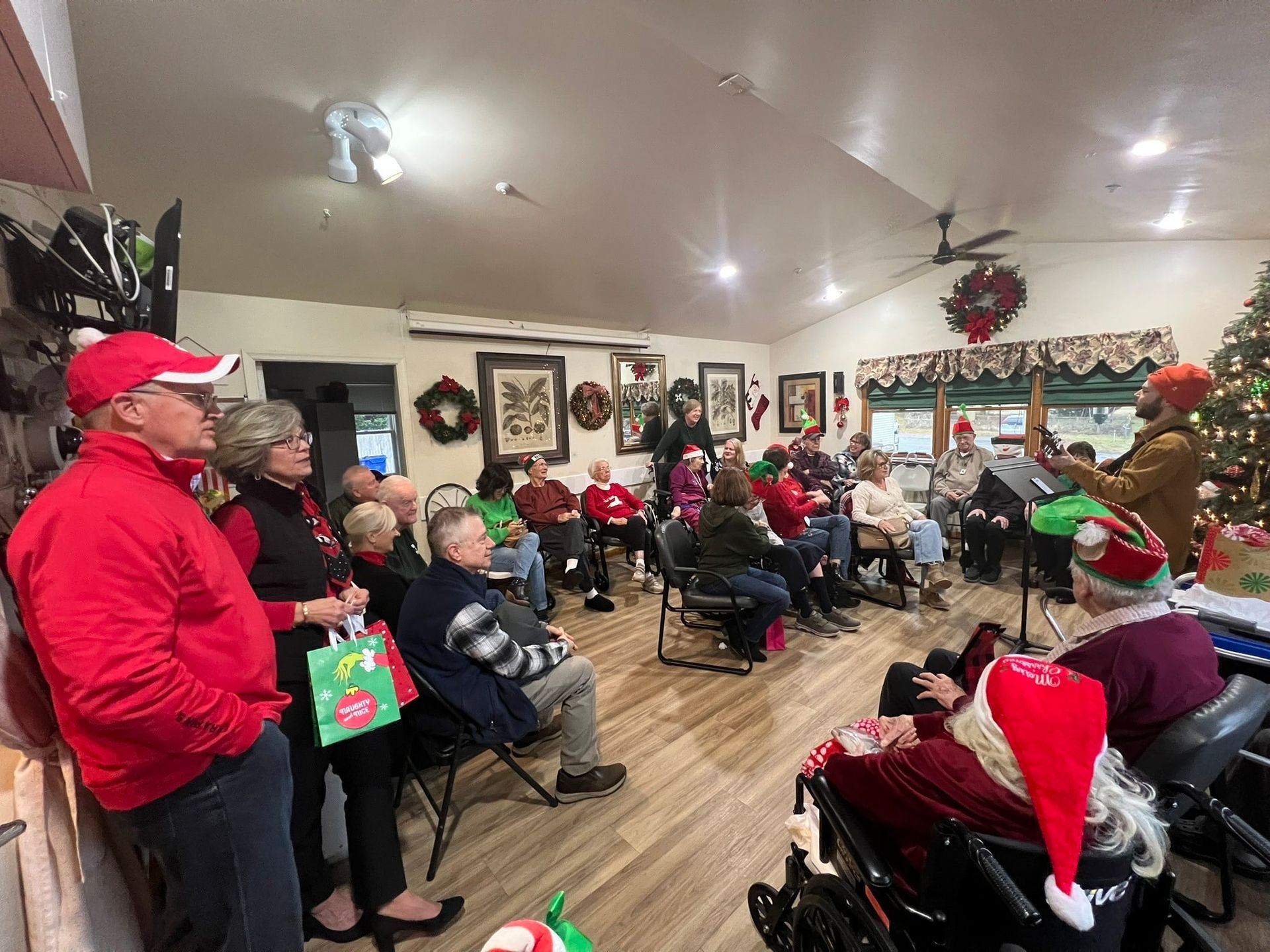 People seated in a festive room with Christmas decorations and Santa hats, watching a holiday gathering
