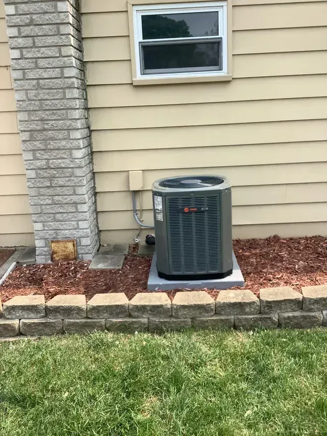 An air conditioner is sitting on the side of a house next to a window.