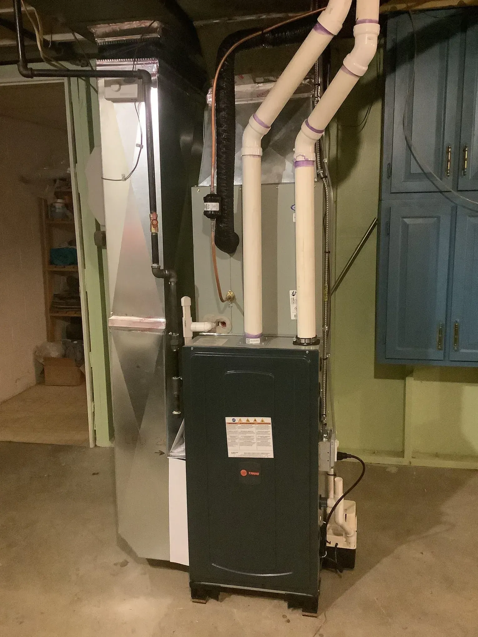 An air conditioner is sitting in a basement next to a blue cabinet.