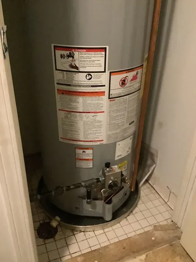 A water heater is sitting on a tiled floor in a room.