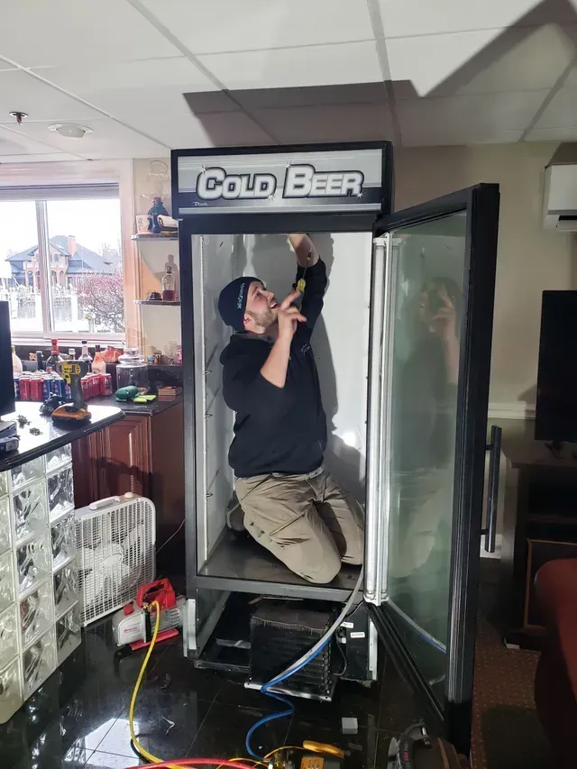 A man is working on a cold beer fridge in a kitchen.