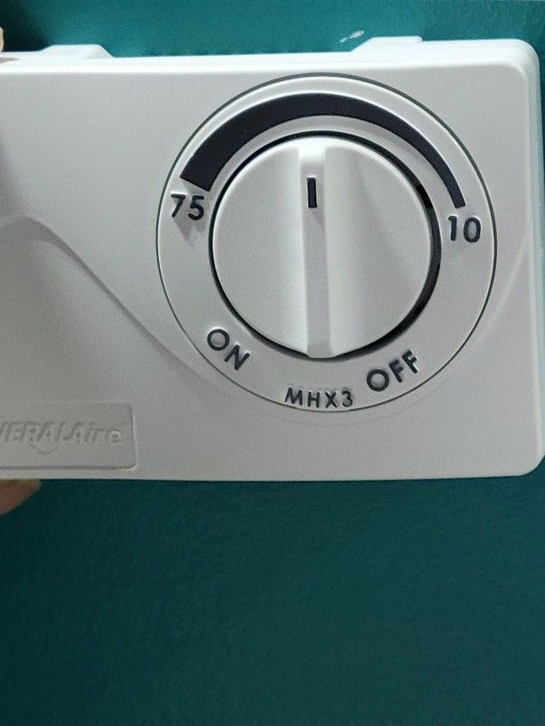 Close-up of a white thermostat dial with ON/OFF and temperature markings on a teal wall Close-up of a white thermostat dial with ON/OFF and temperature markings on a teal wall
