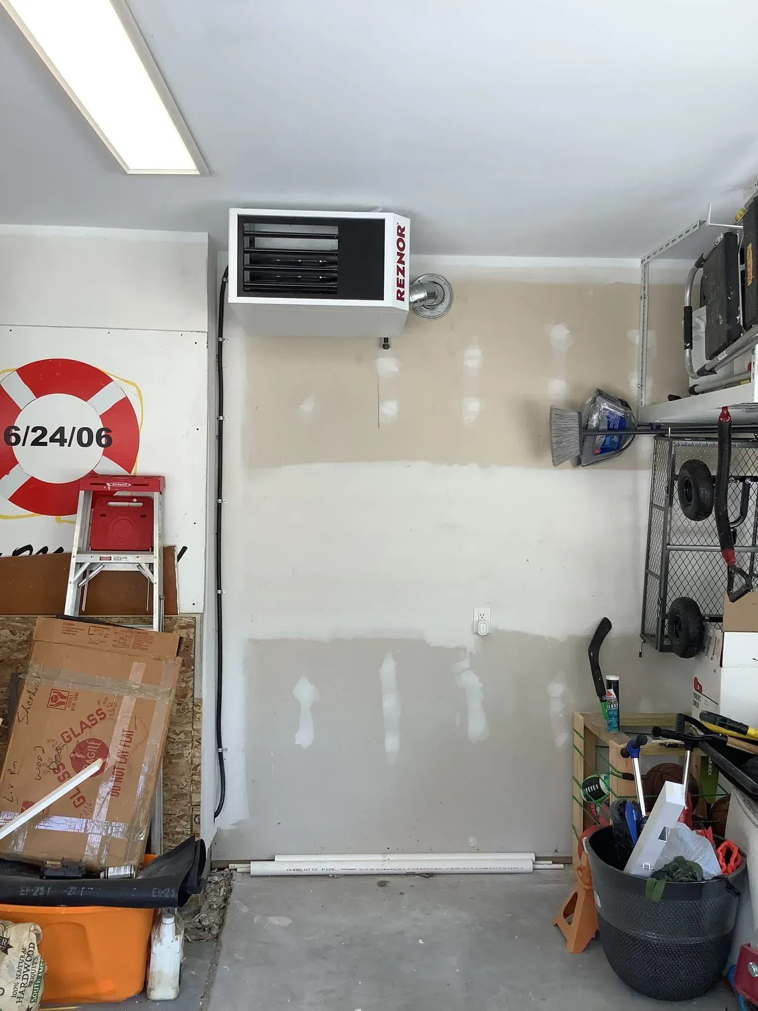 A garage with a heater hanging from the ceiling and a life preserver on the wall.