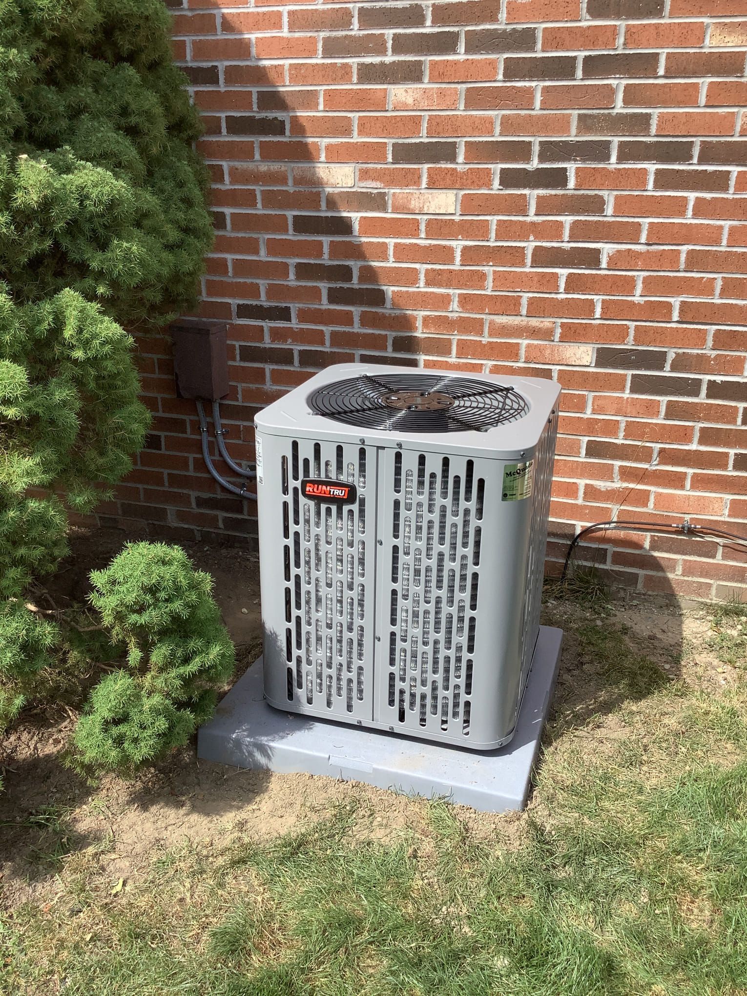 Efficient Goodman outdoor AC unit next to brick wall at Rochester Hills HVAC client home.