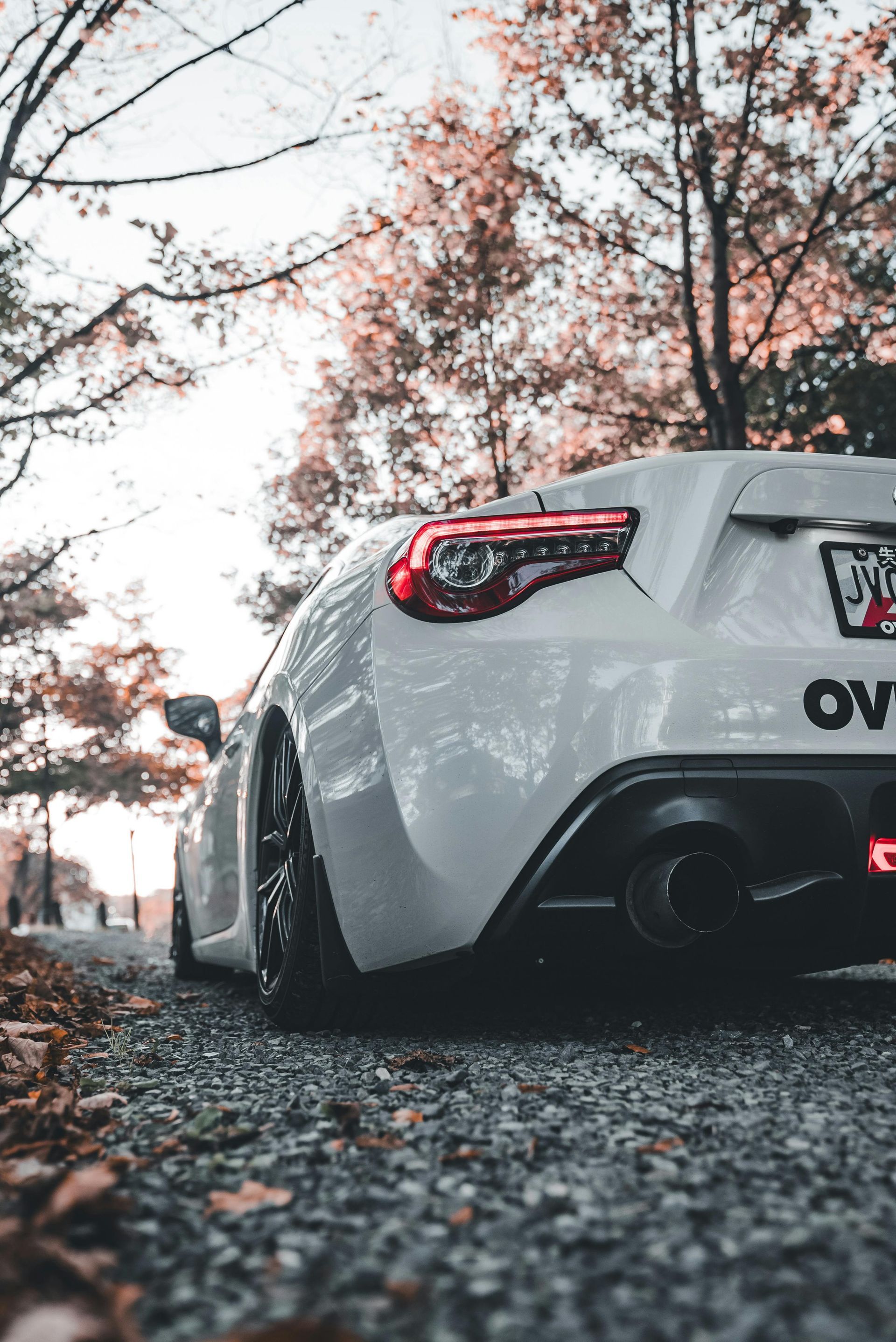 A white sports car is parked on the side of a gravel road.
